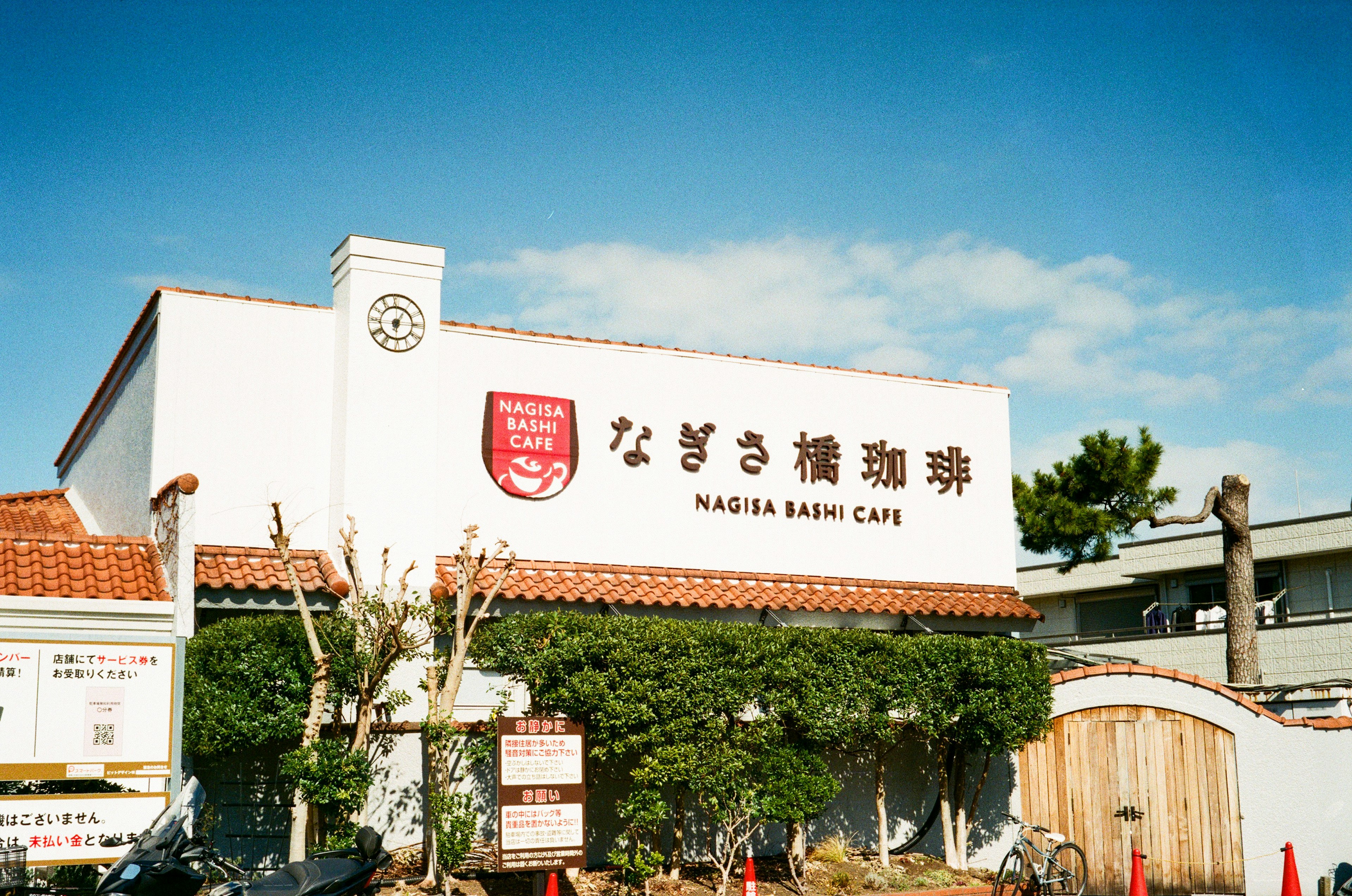 Extérieur du Nagisa Bakery Cafe sous un ciel bleu murs blancs et toit rouge