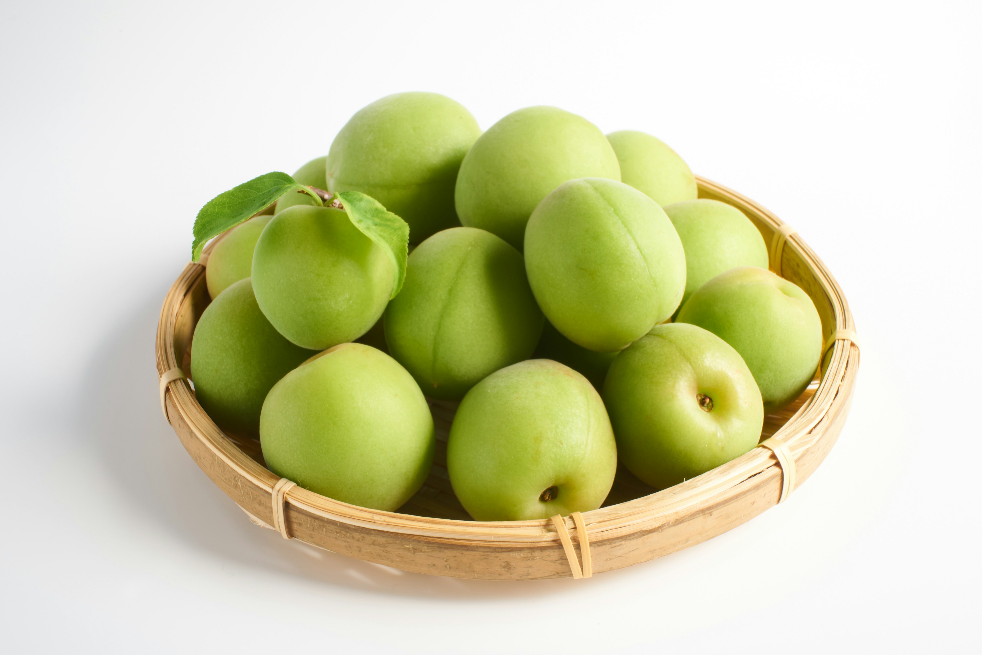 Ciruelas verdes dispuestas en una canasta de bambú