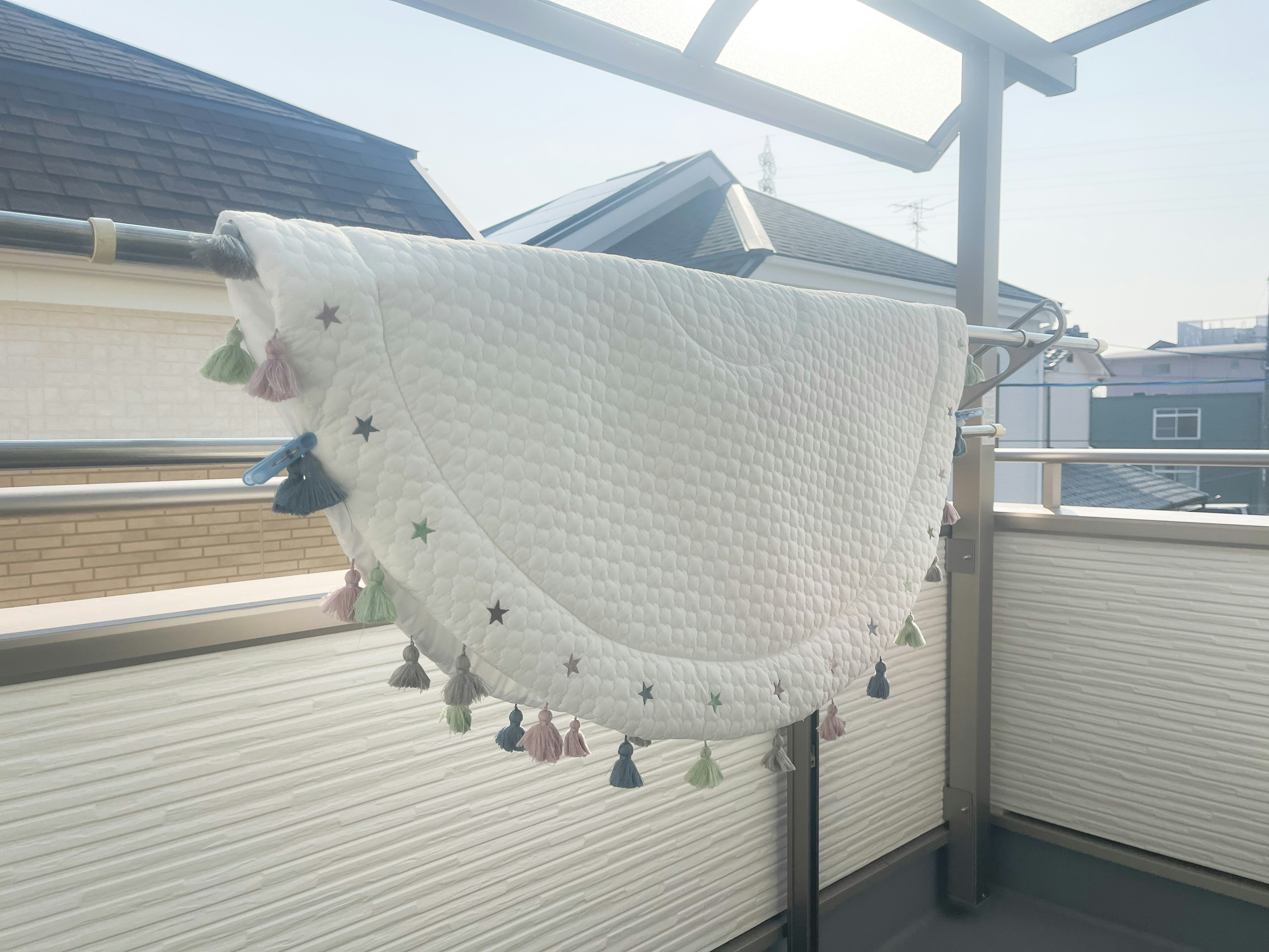 A white blanket hanging on a balcony with colorful tassels along the edge