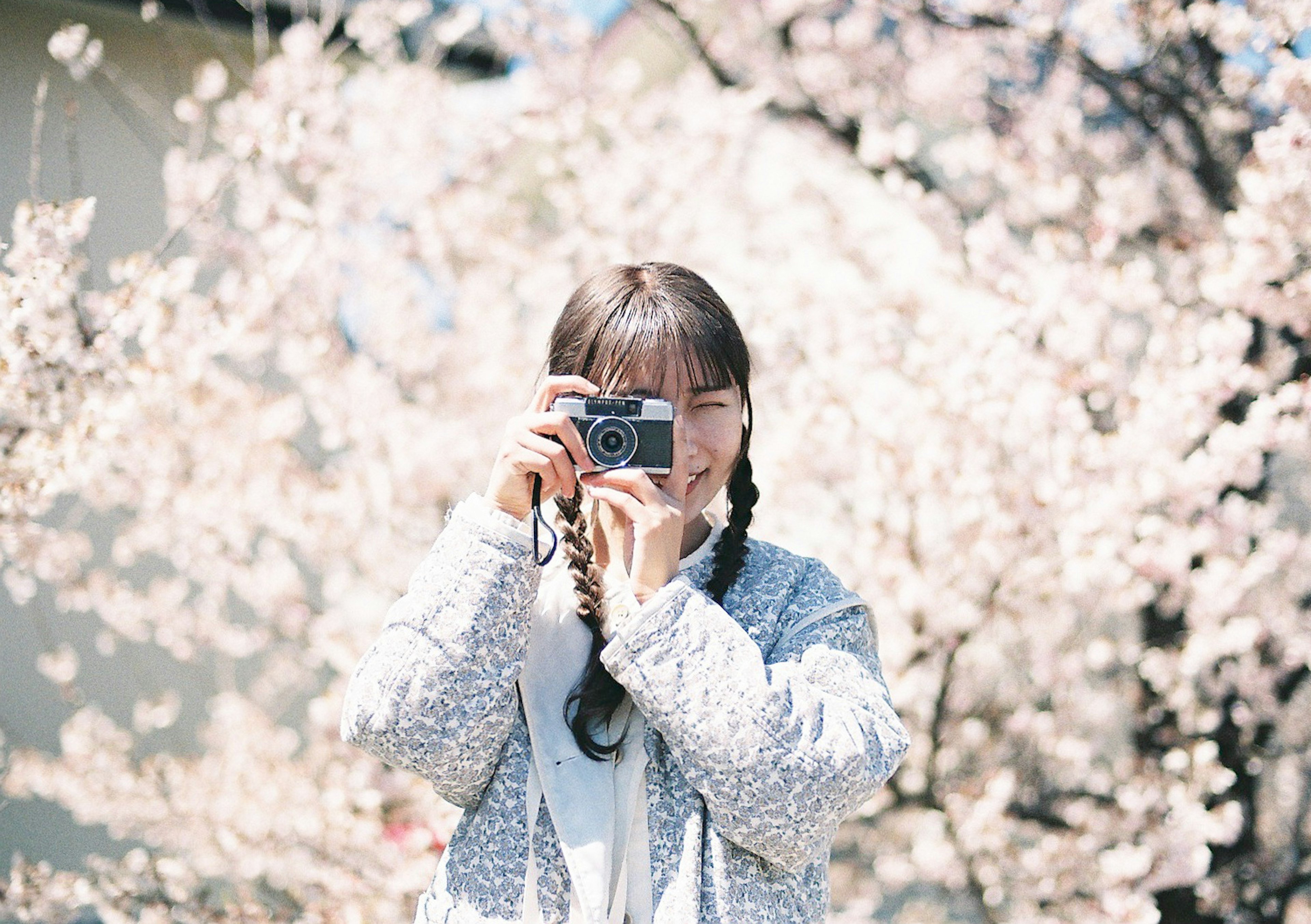 Femme souriante tenant un appareil photo devant des cerisiers en fleurs