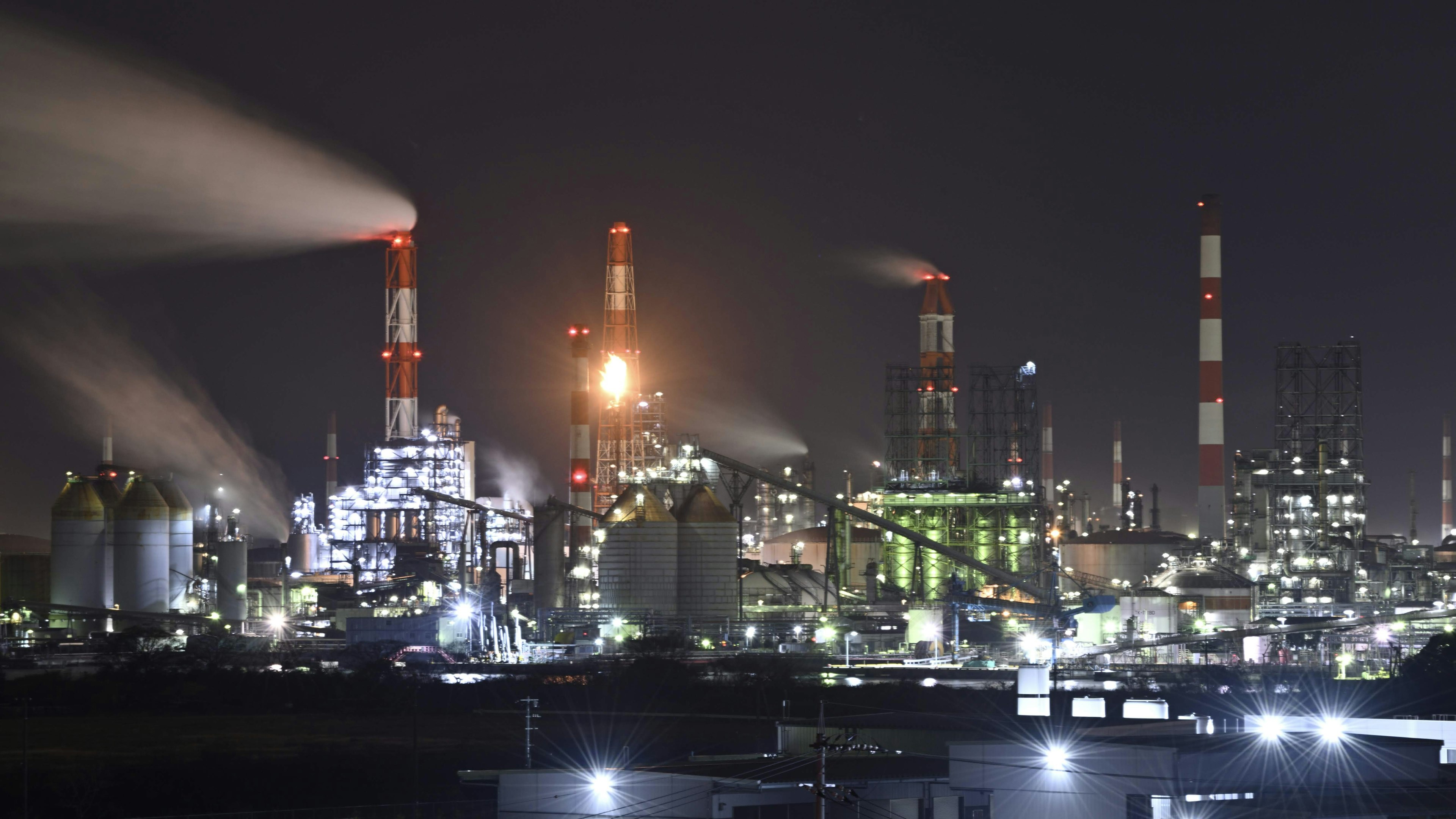 Night view of an industrial area with smokestacks emitting smoke and bright factory lights