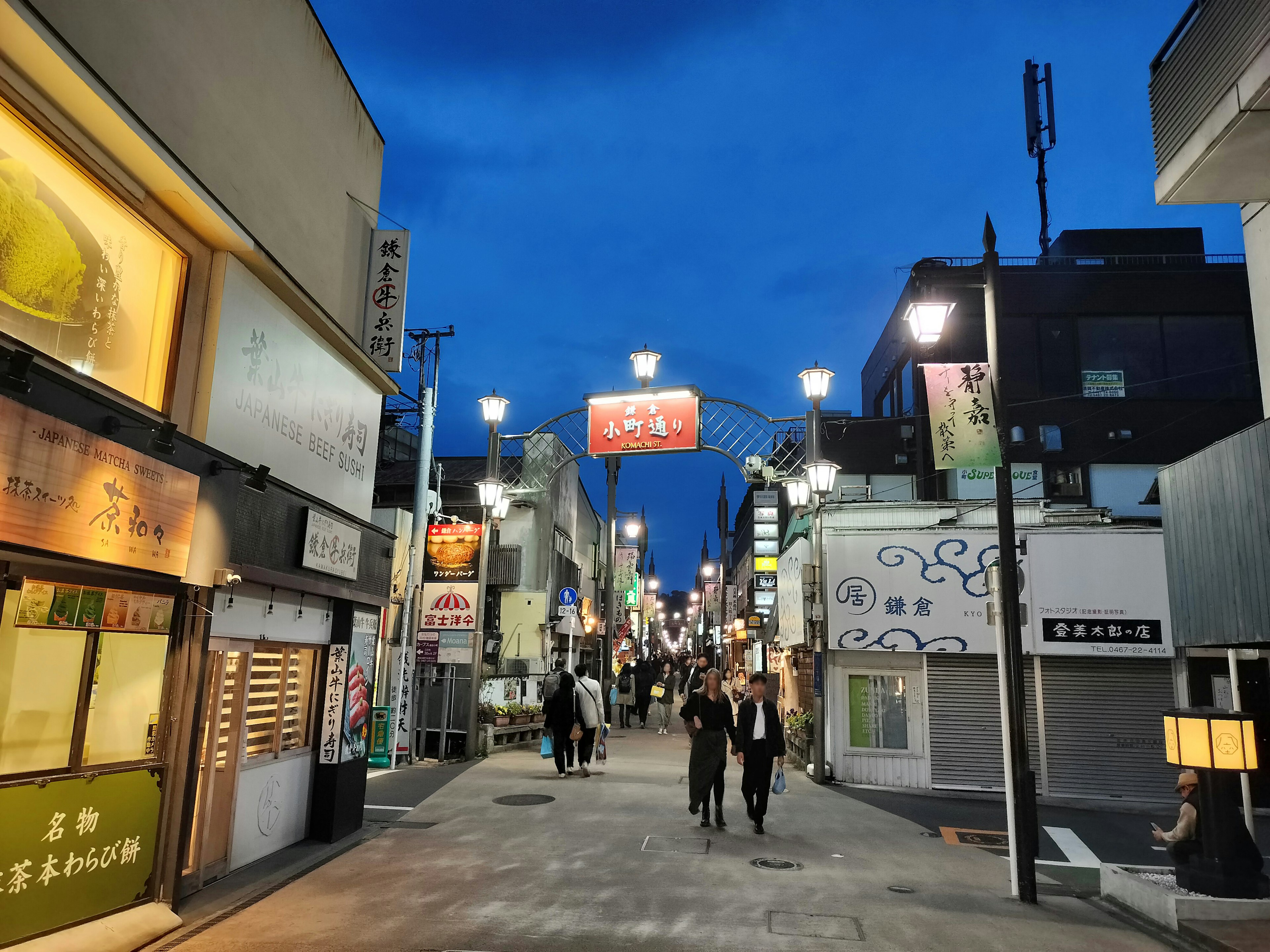 Calle concurrida con personas caminando de noche bajo un cielo azul