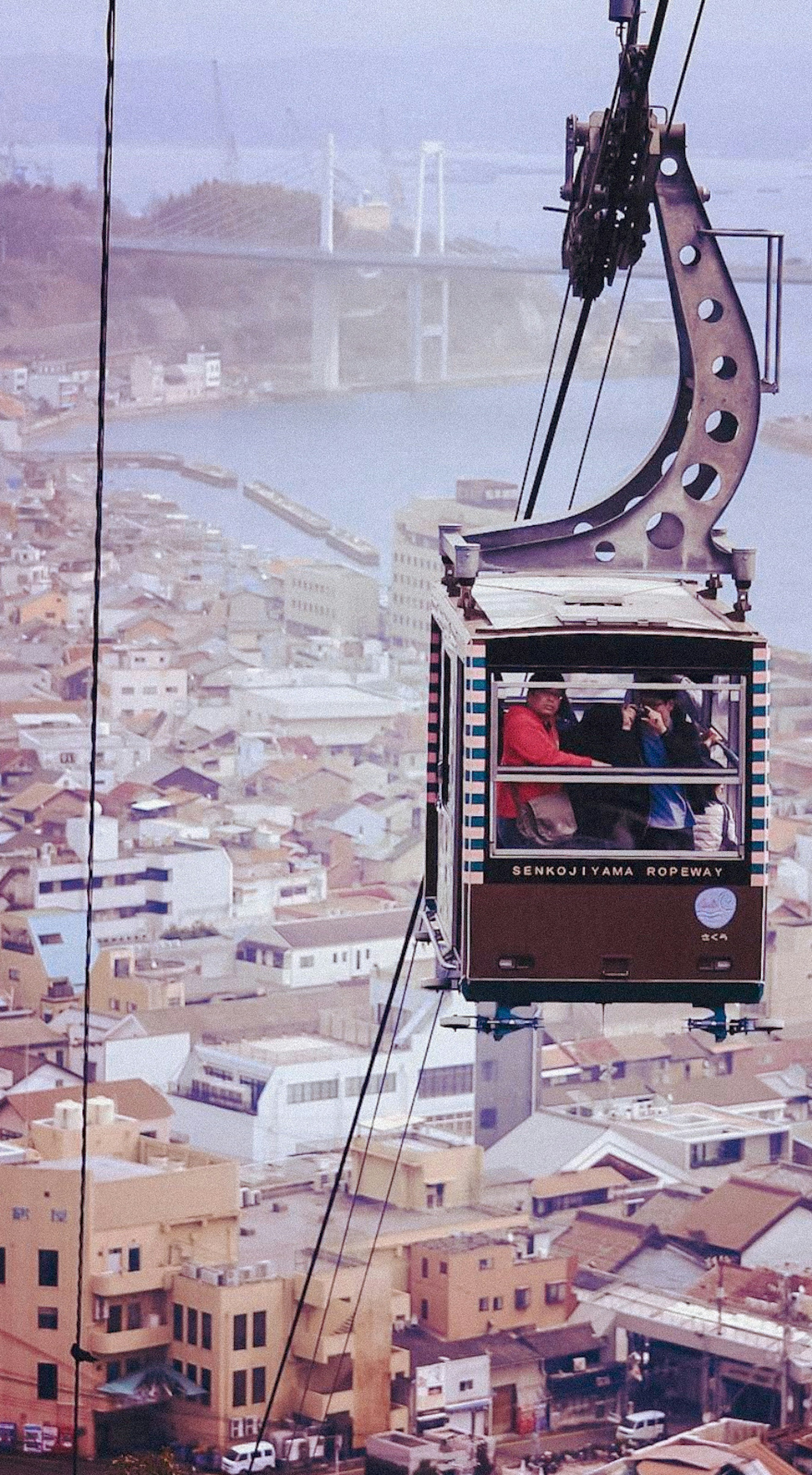 Eine Seilbahn, die über eine Stadtlandschaft mit Gebäuden und einem Gewässer im Hintergrund fährt