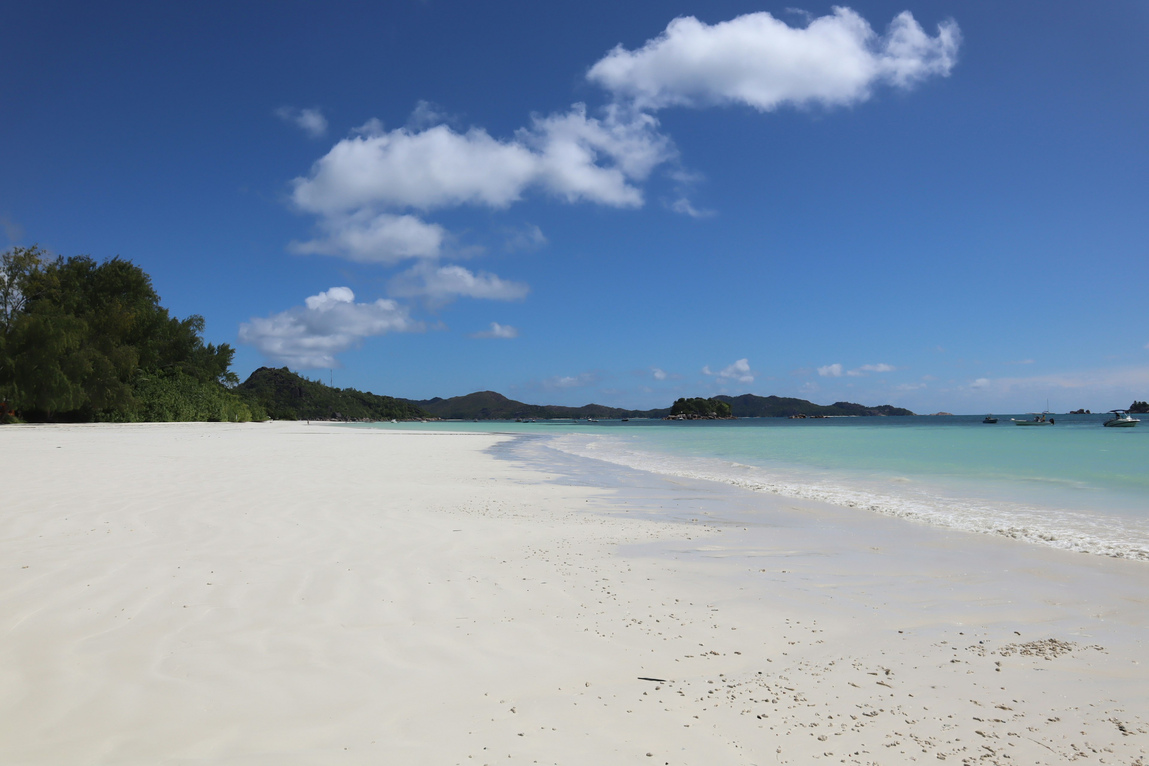 ชายหาดที่มีทรายขาวและน้ำสีฟ้าเขียวใต้ท้องฟ้าสีฟ้าใส