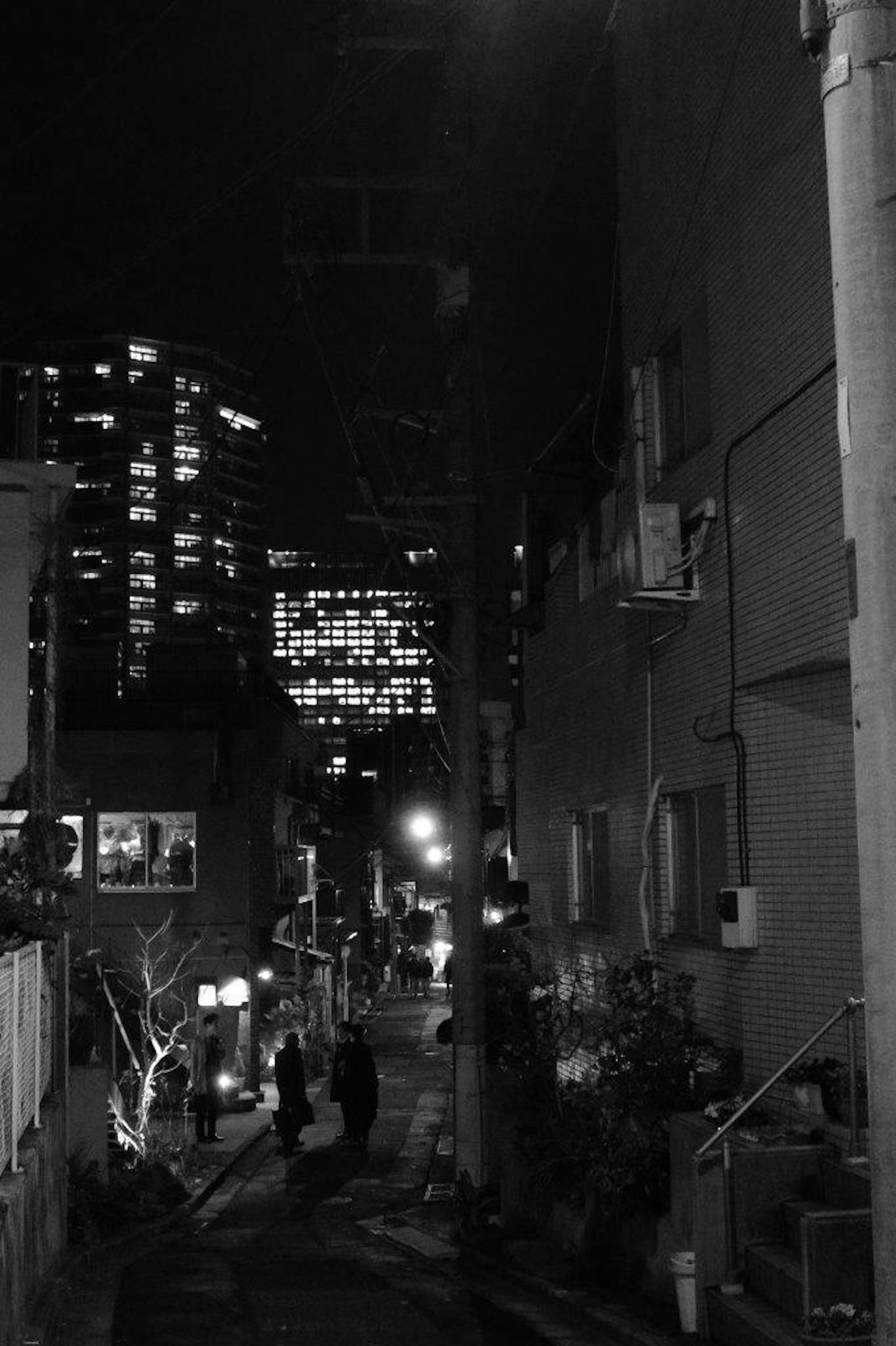 Photo en noir et blanc d'une ruelle étroite la nuit avec des personnes marchant