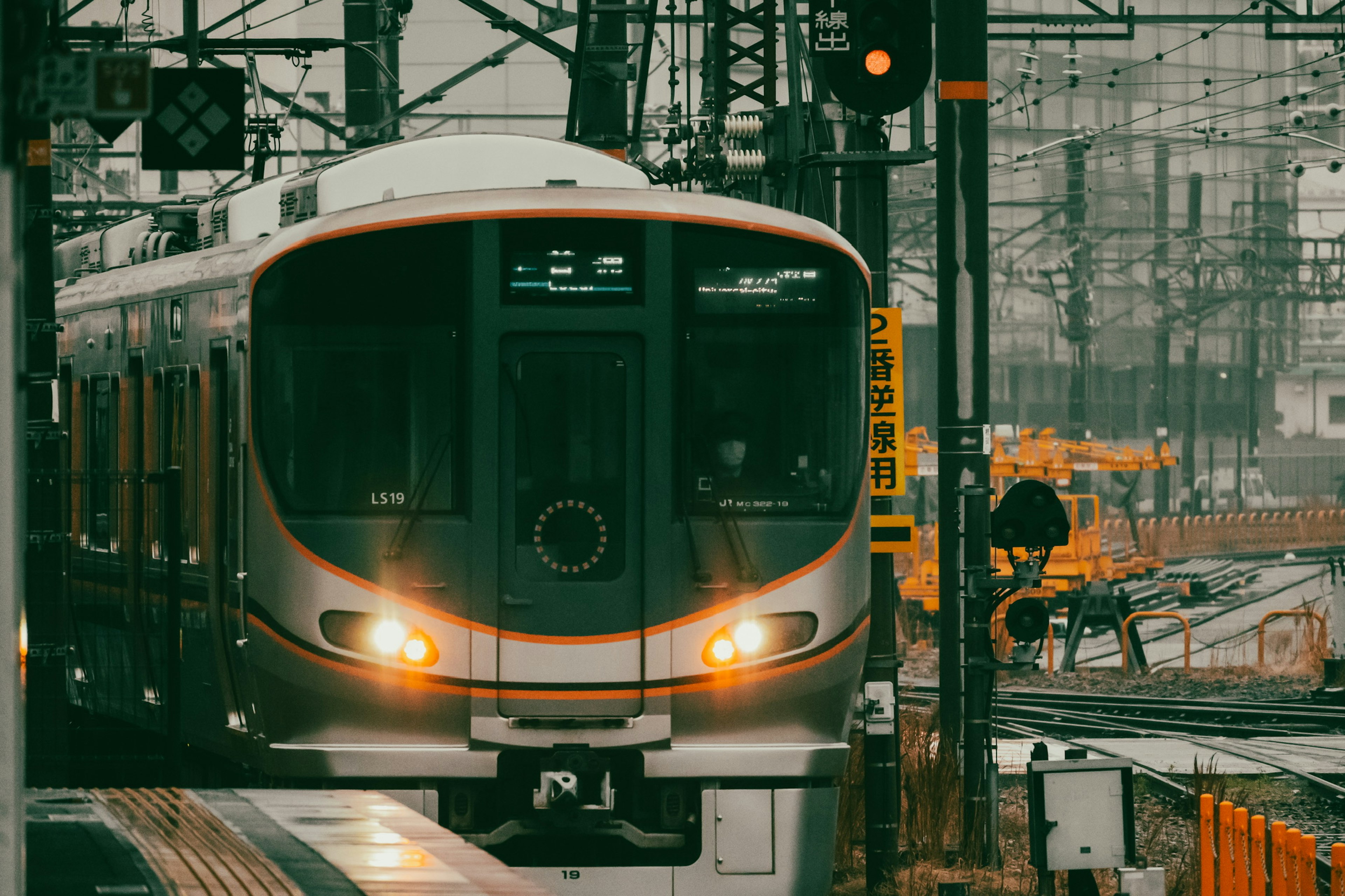 Treno in arrivo a una stazione con infrastrutture ferroviarie e binari circostanti