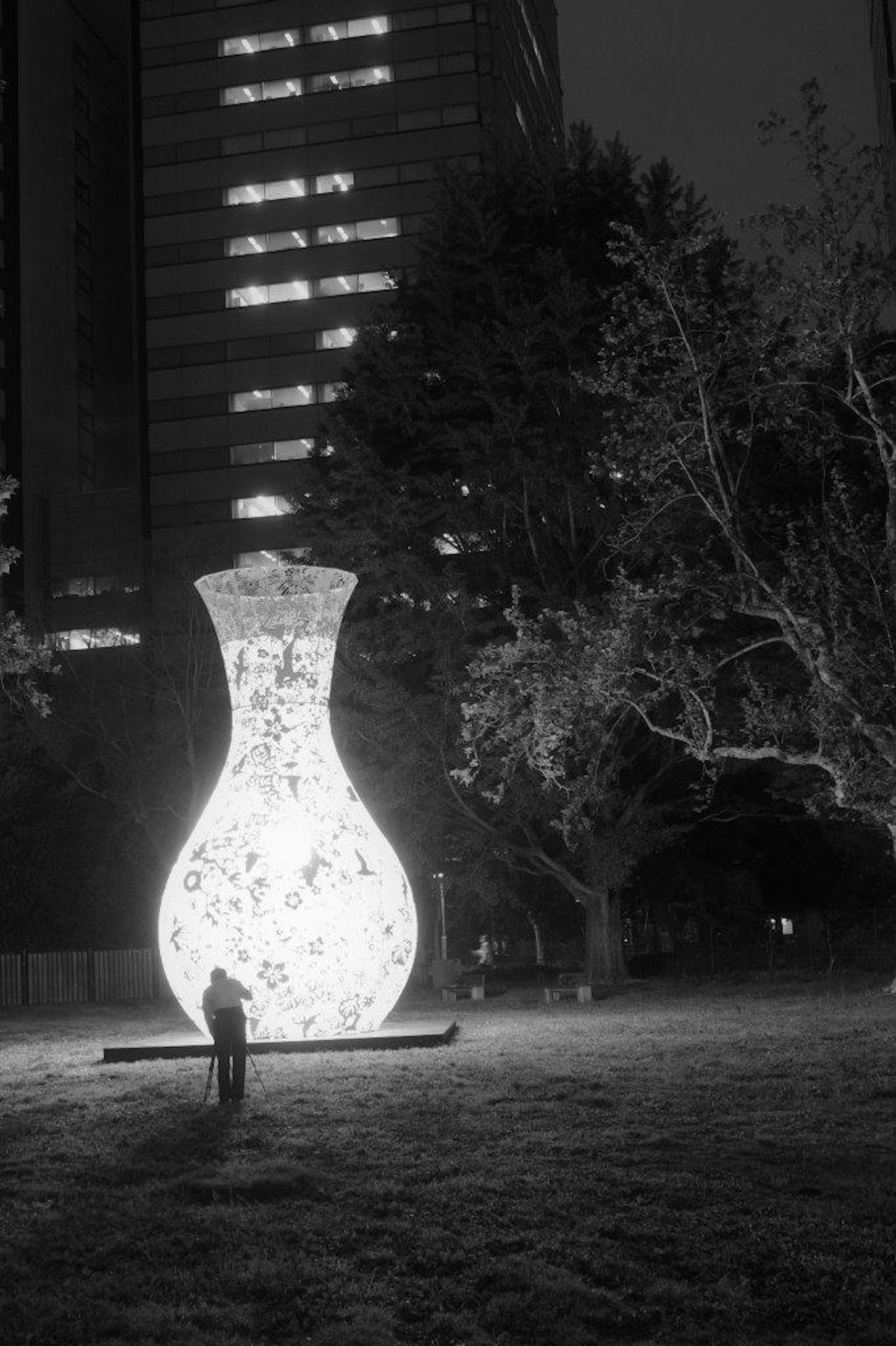 Große Kunstinstallation in Form einer weißen Vase in einem Park bei Nacht mit einer Person in der Nähe