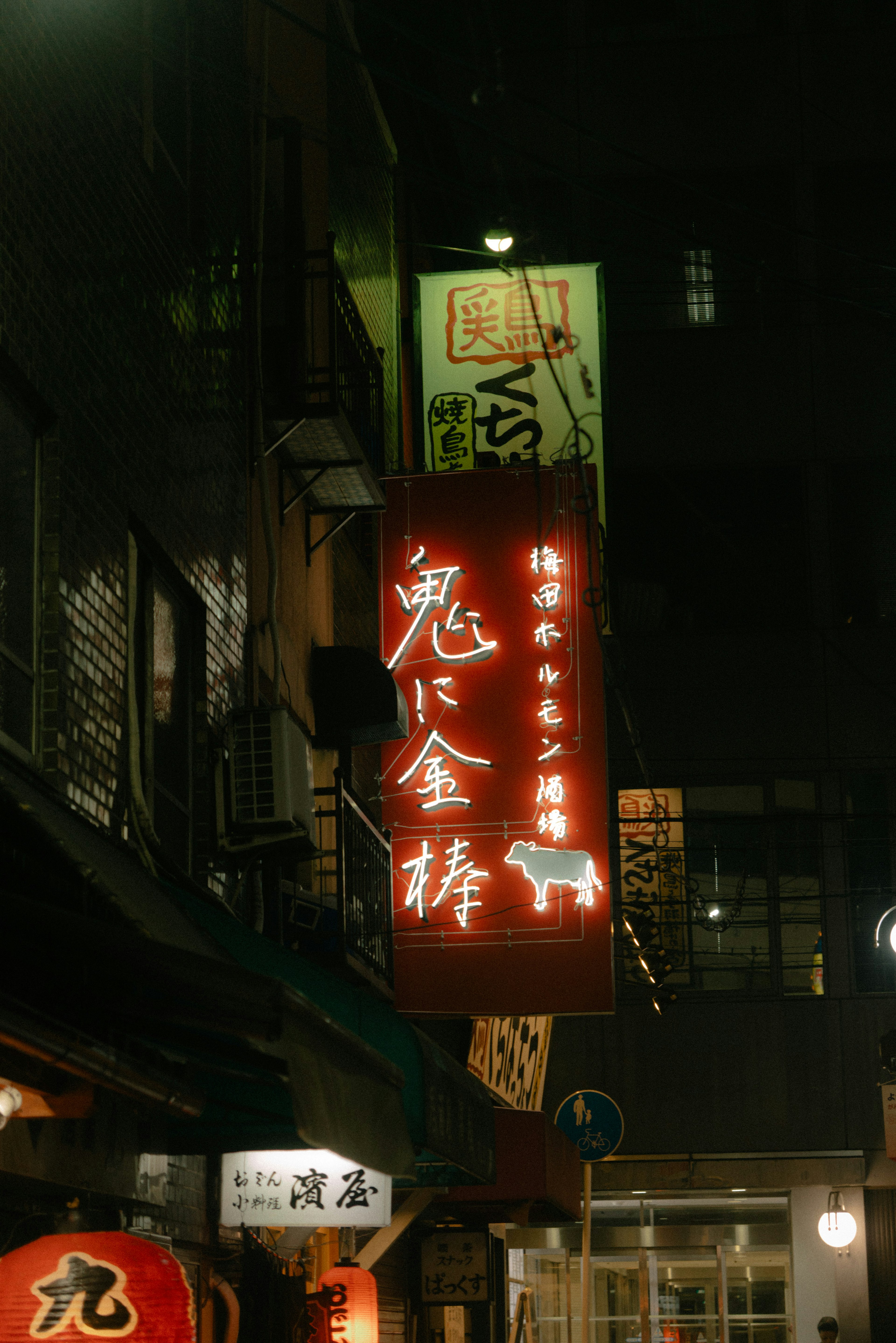 Panneau rouge illuminé d'un izakaya avec le nom Oni ni Kanabo la nuit