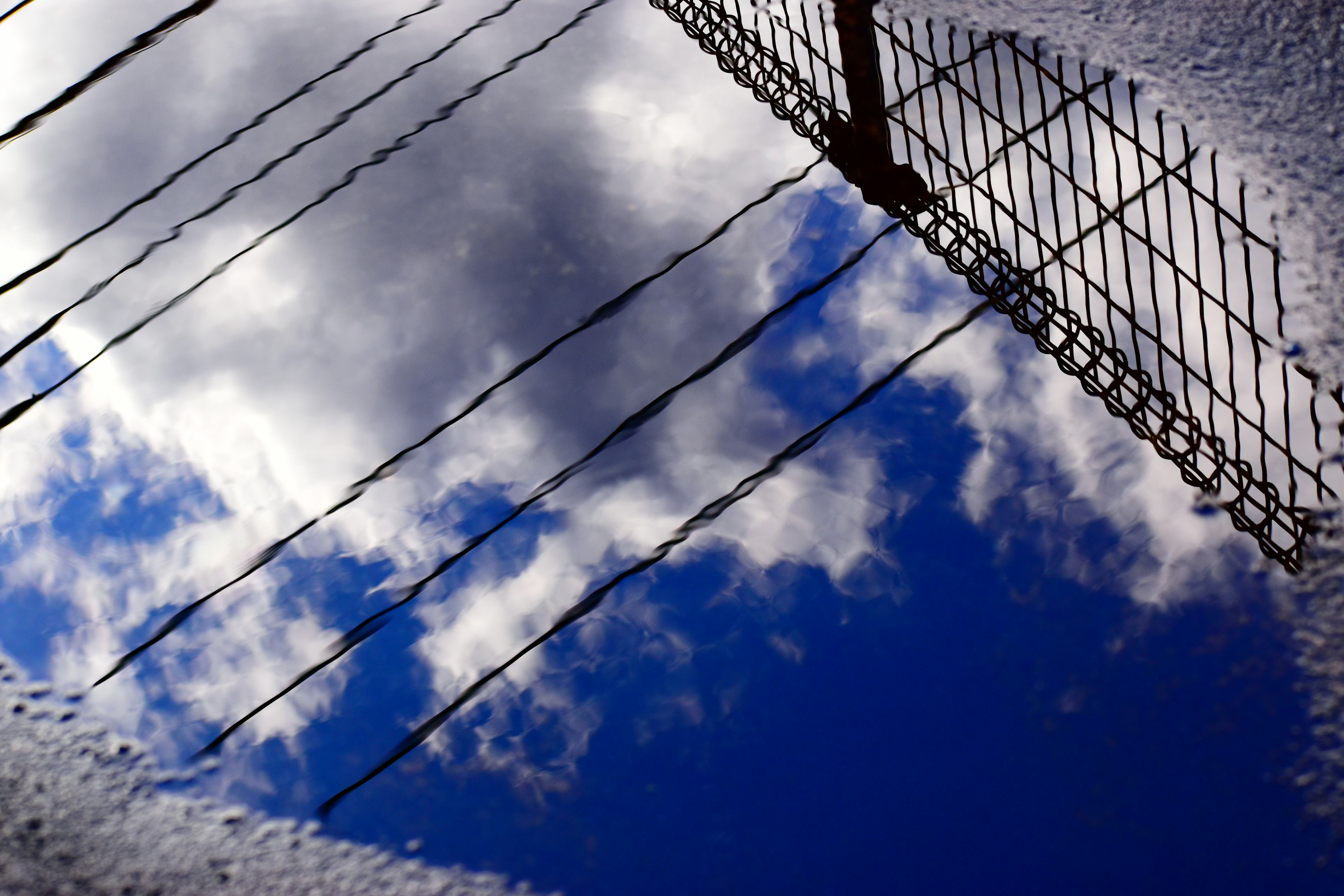 Réflexion du ciel bleu et des nuages dans une flaque avec l'ombre d'une clôture