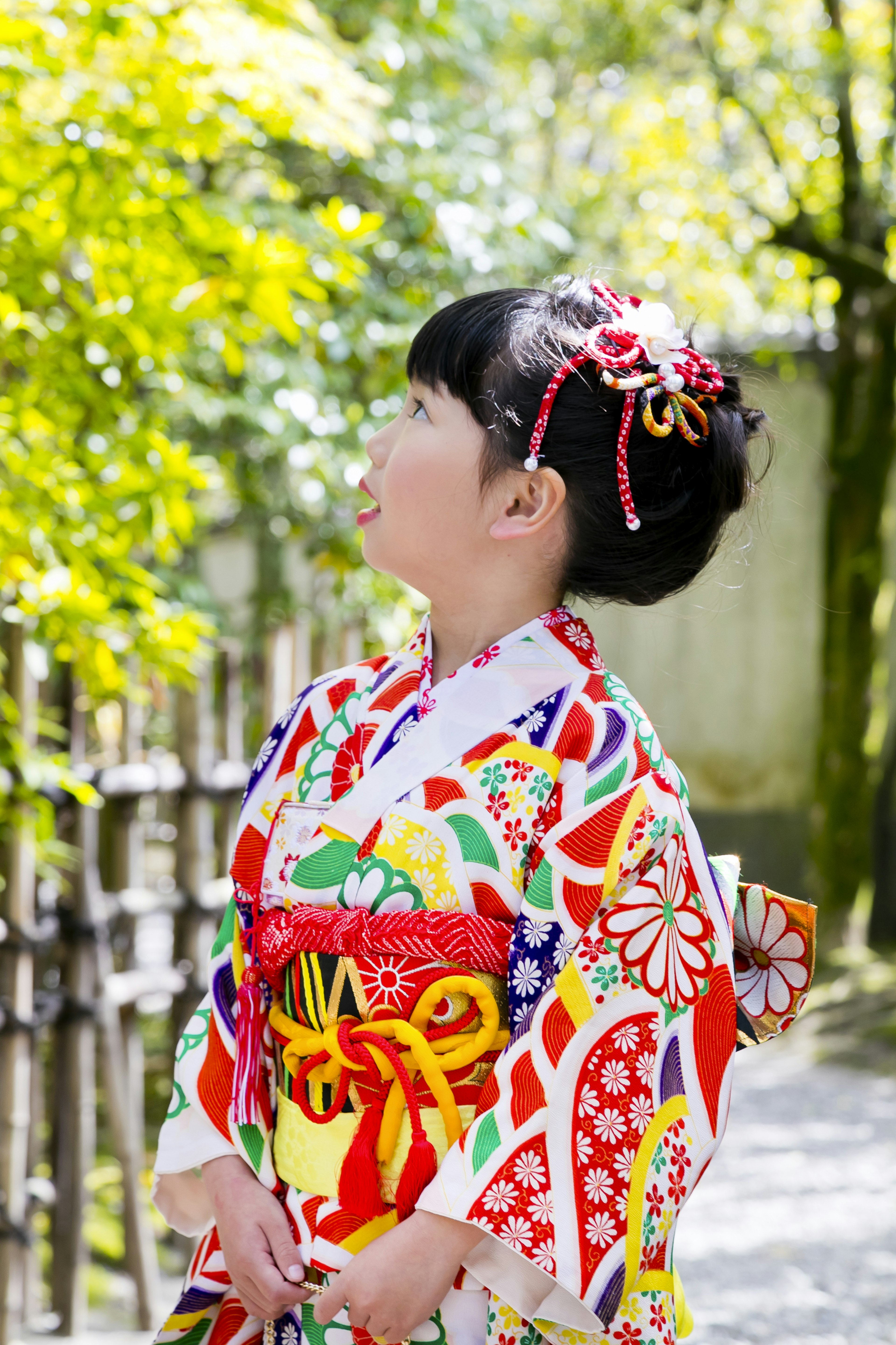 Ein Mädchen in einem bunten Kimono schaut zu den grünen Bäumen hoch