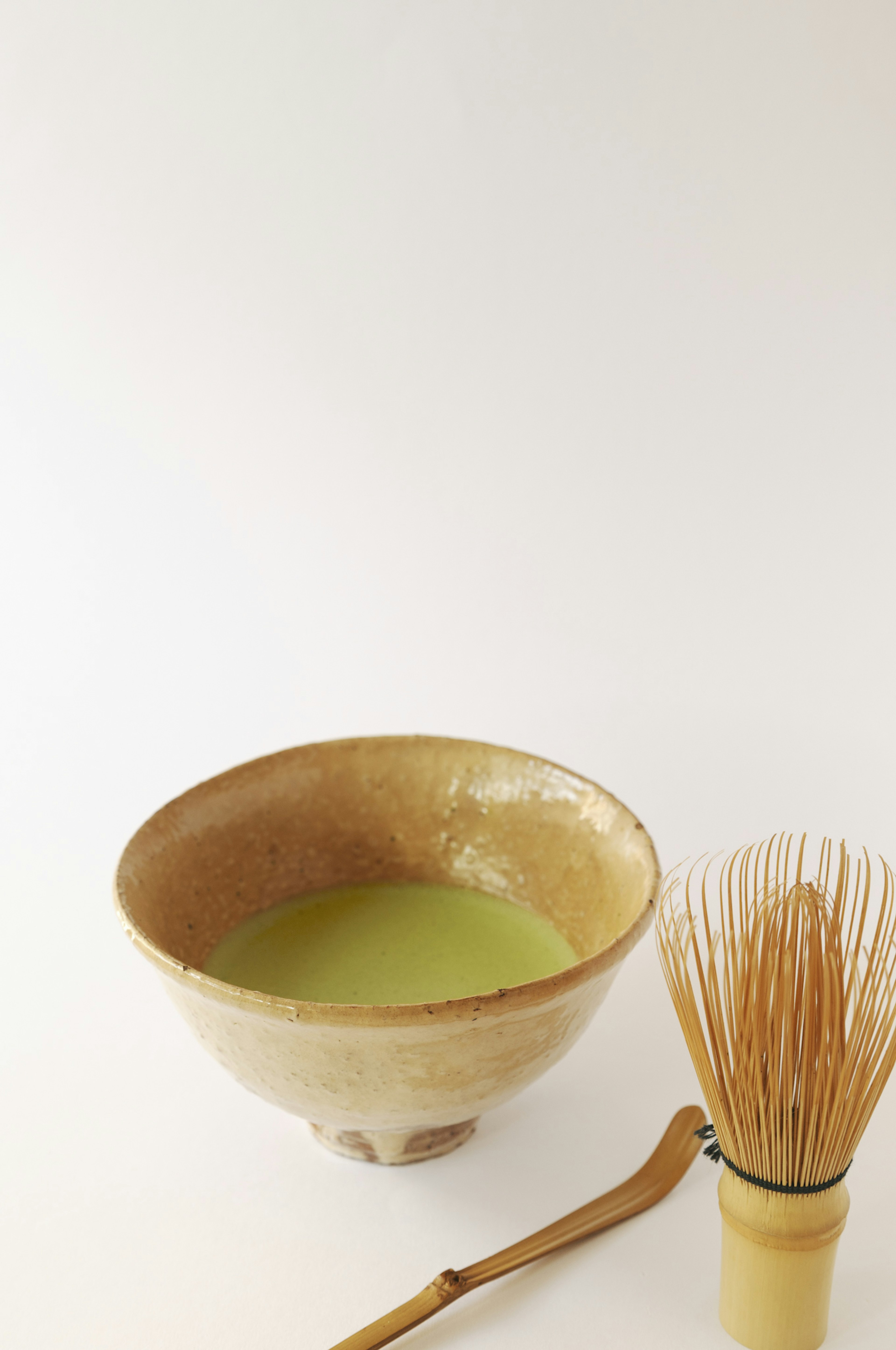 Image of a ceramic bowl filled with green matcha tea and a bamboo whisk