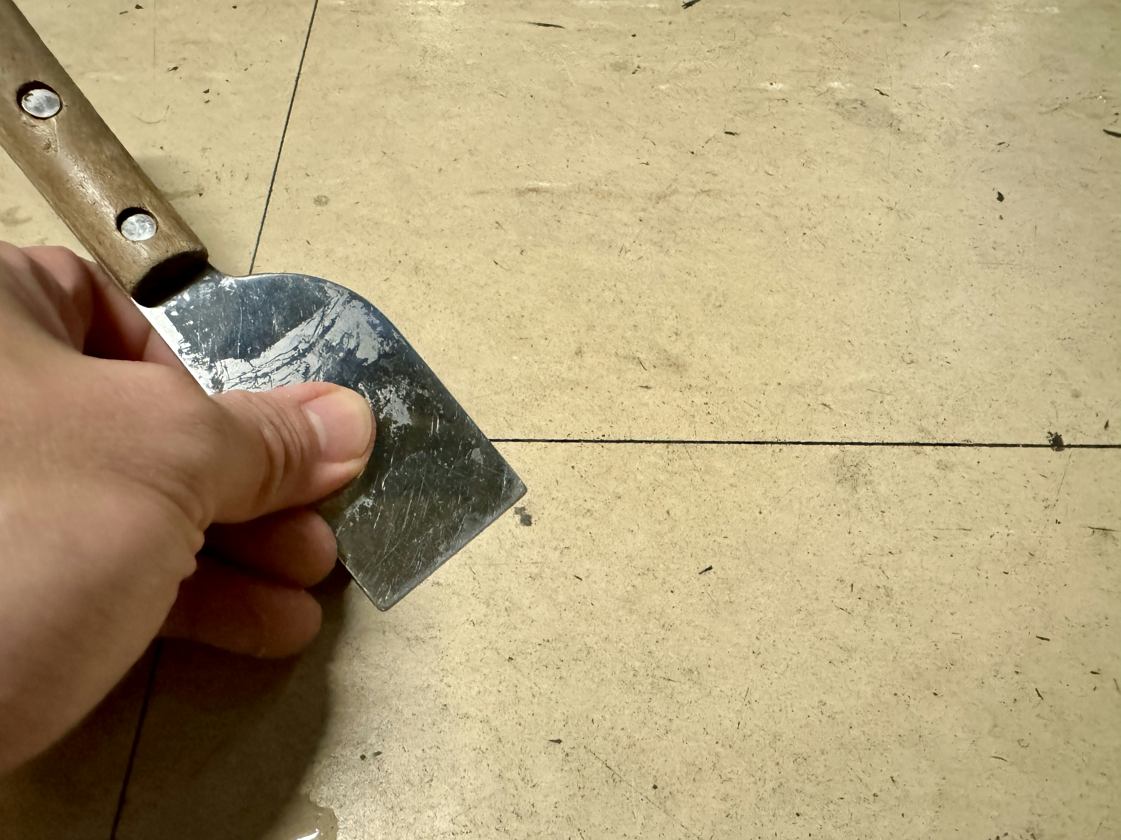 A metal scraper held in hand directed towards a floor