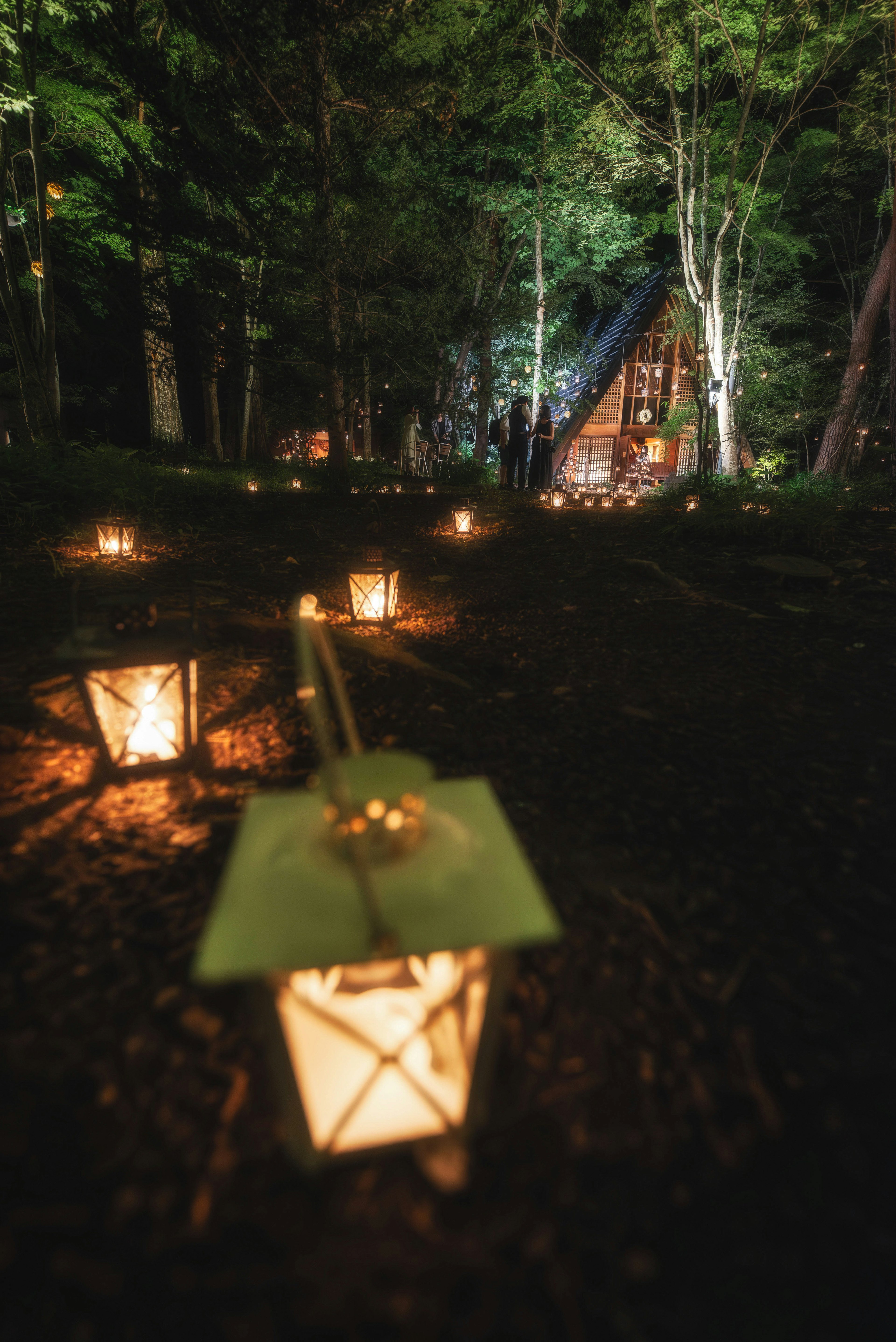 夜の森に並ぶランタンと小屋の風景