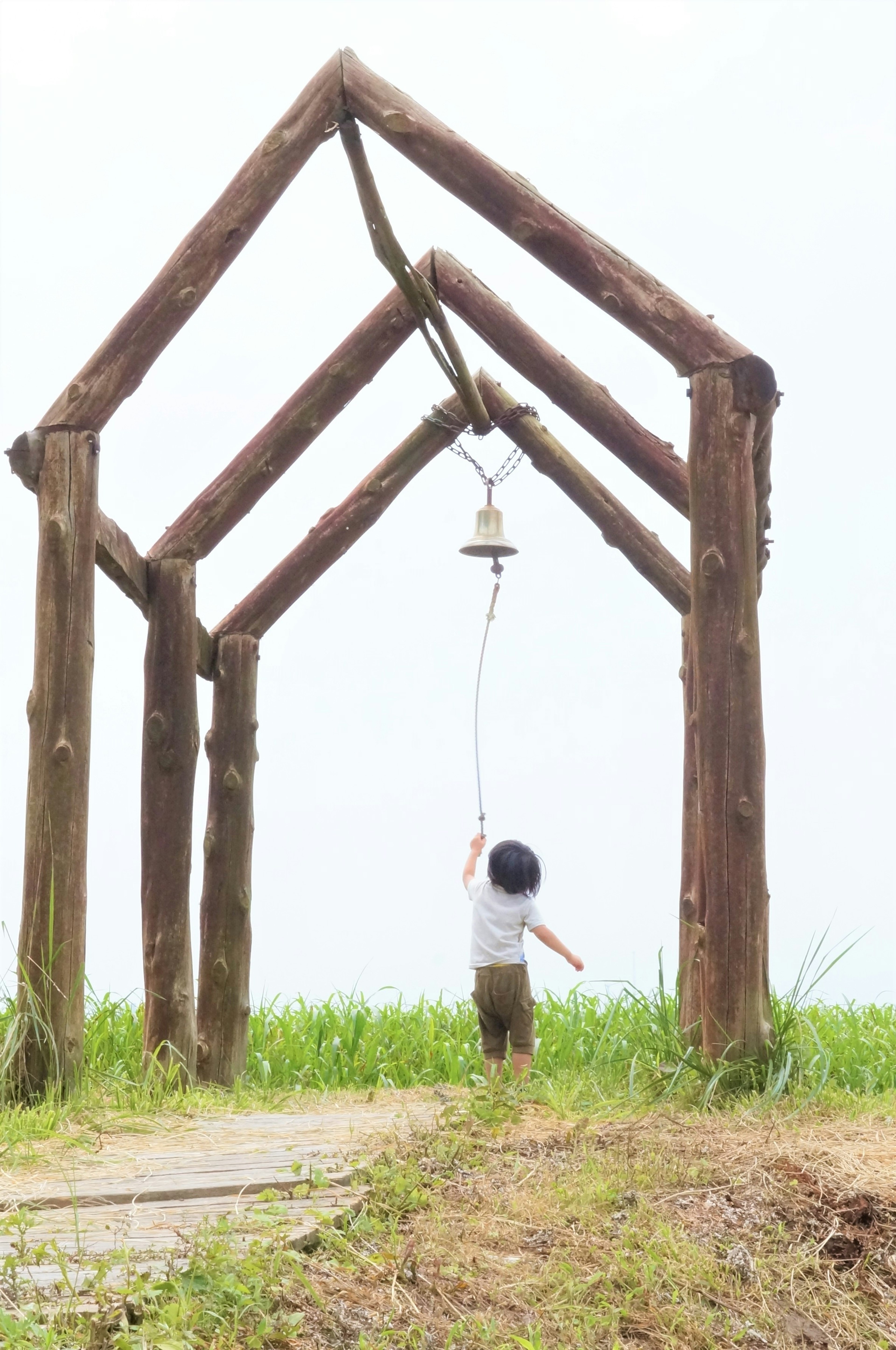 Seorang anak membunyikan lonceng di bawah struktur lengkung kayu