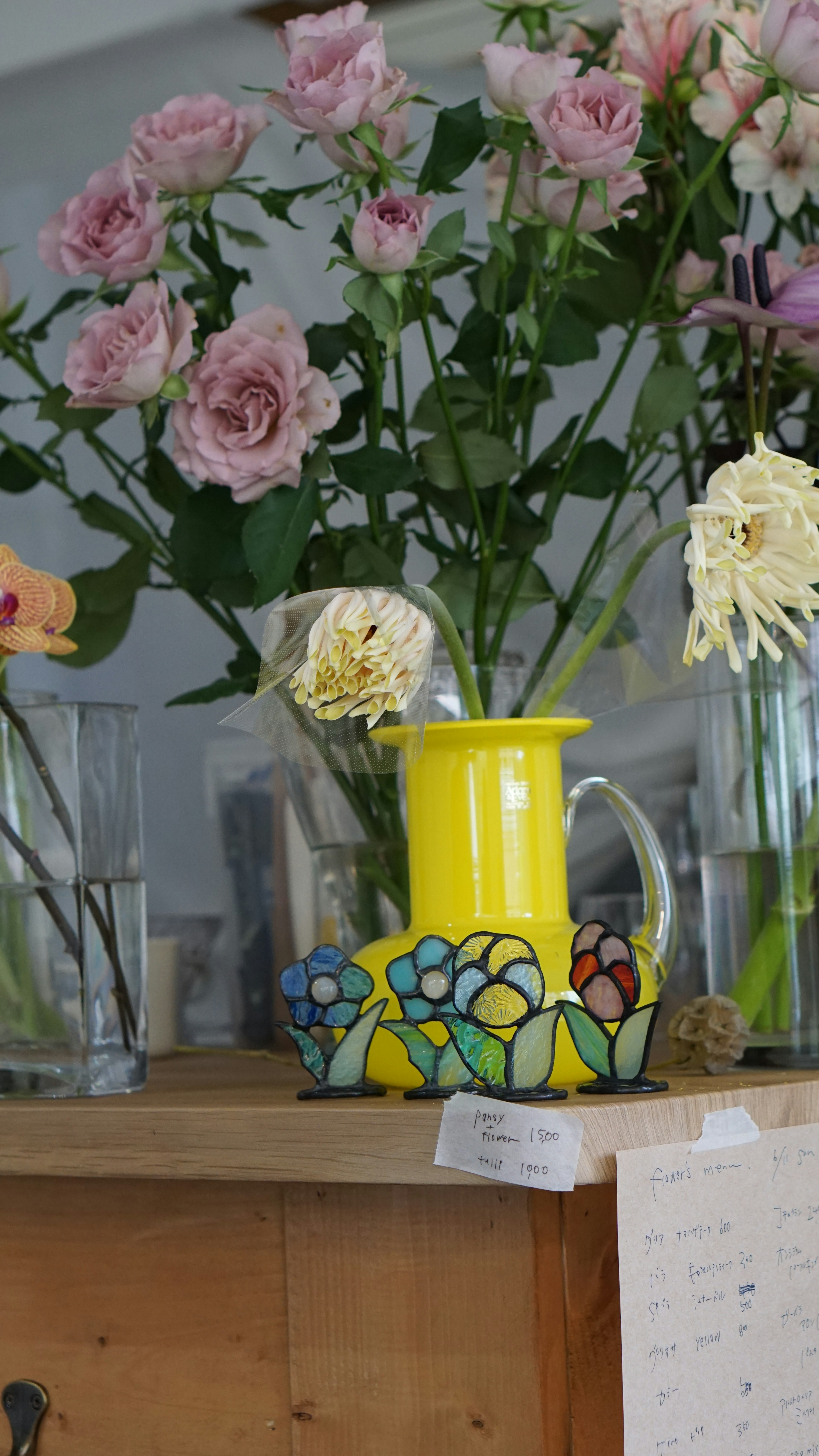 Una jarra amarilla vibrante con un diseño floral colorido se encuentra sobre una mesa rodeada de rosas rosas y otras flores