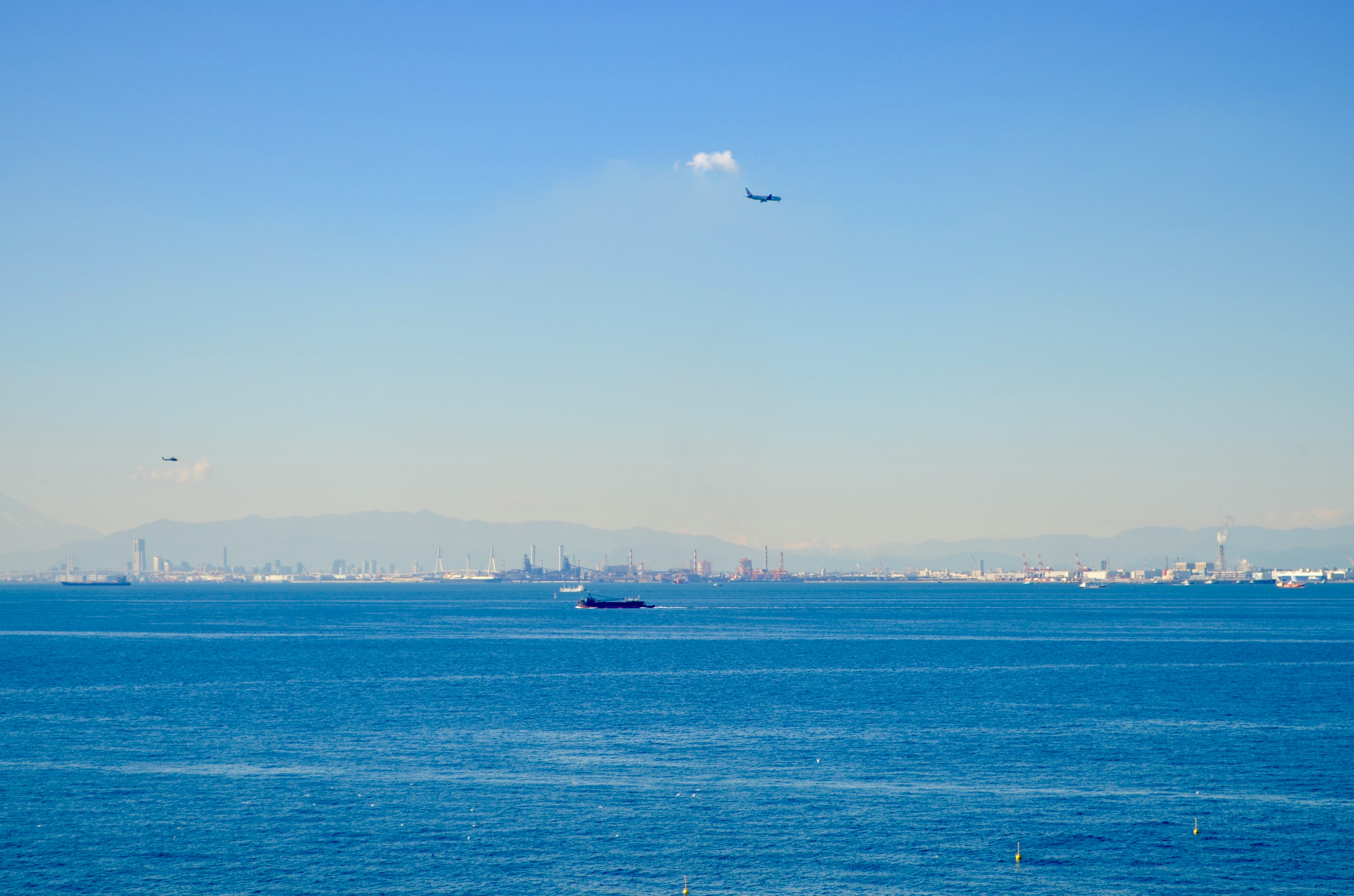 A view of blue ocean with a city skyline in the distance and planes flying overhead