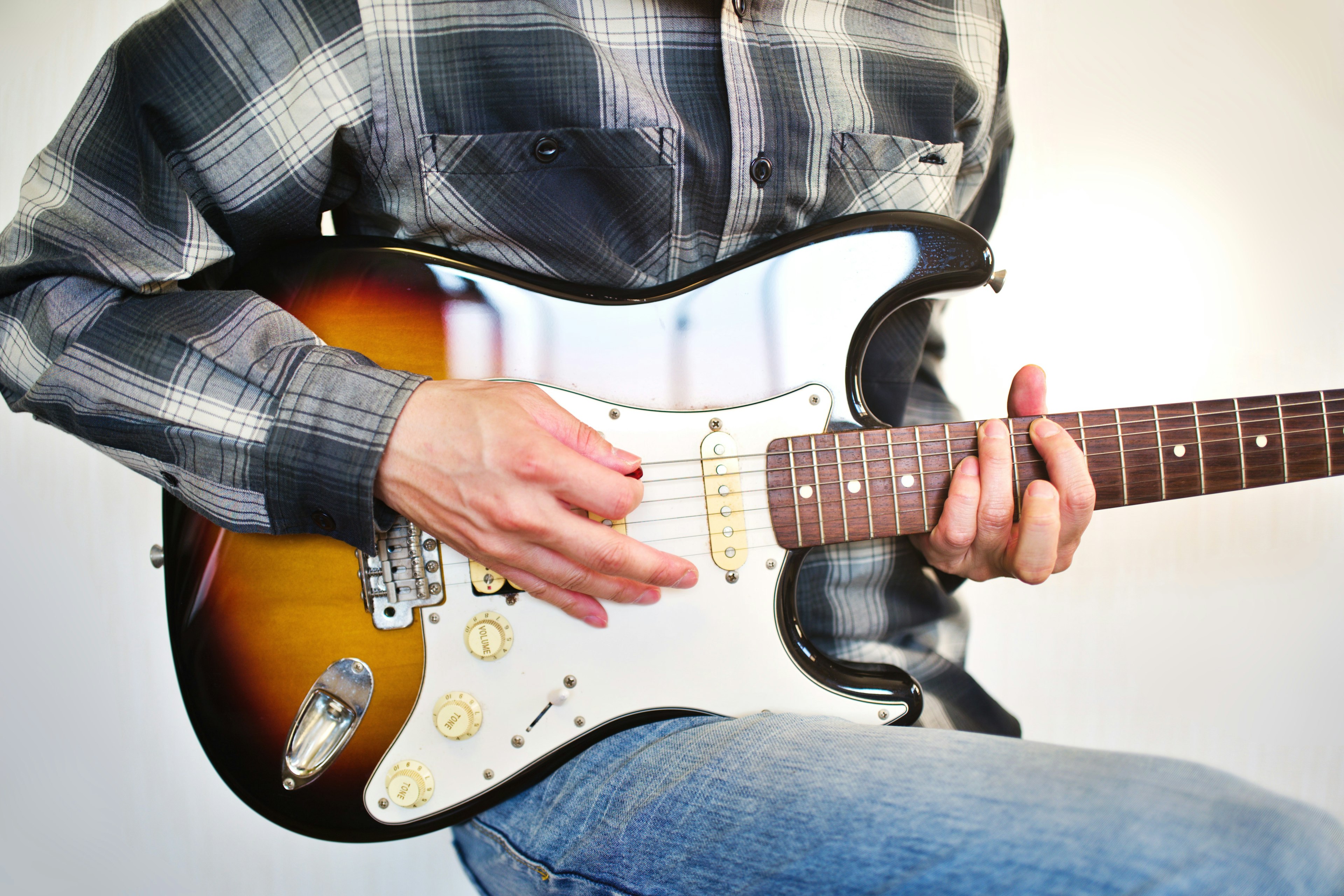 A person playing a Stratocaster guitar with hands on the fretboard