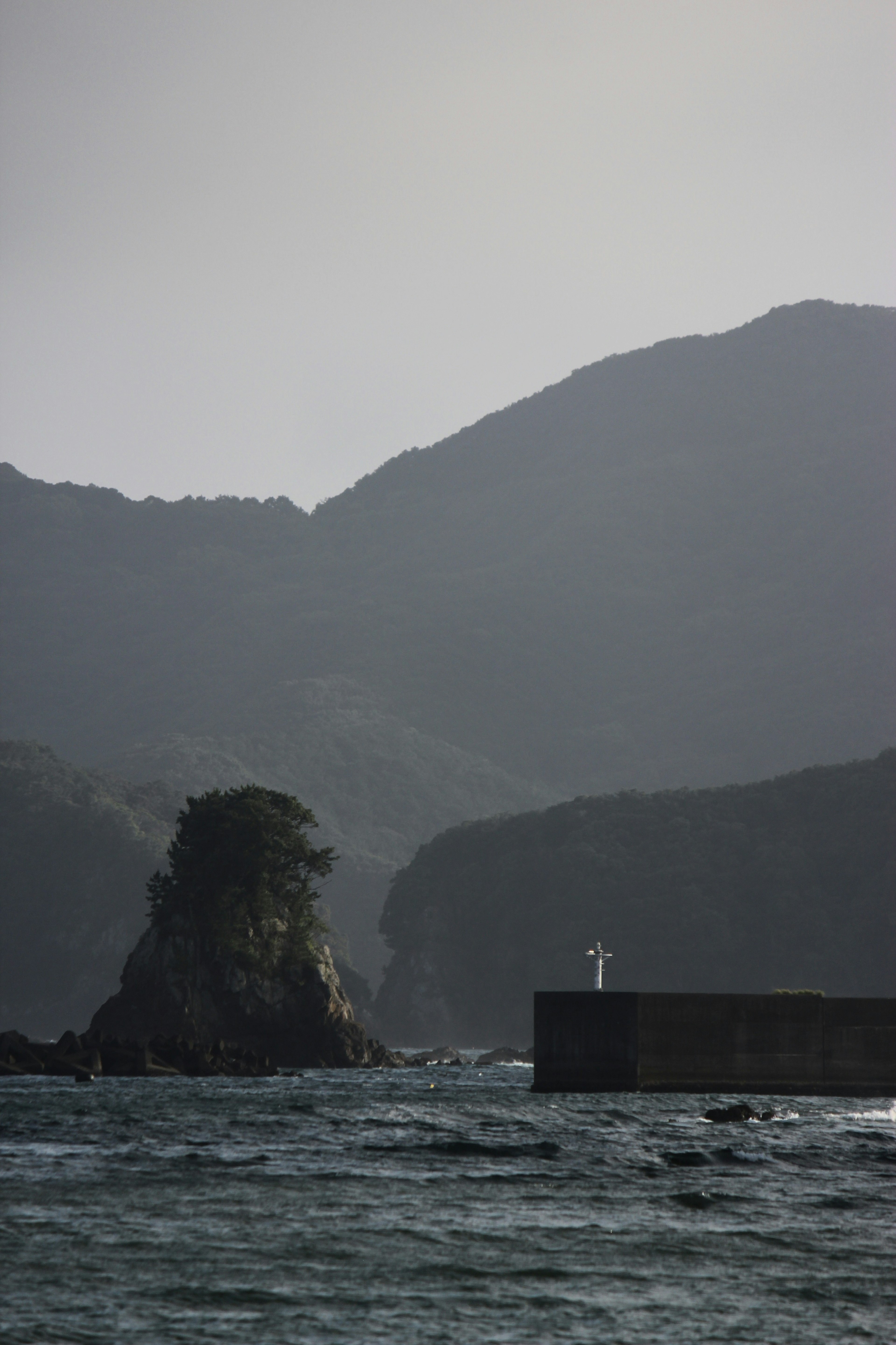 Lighthouse on a pier with rocky island and mountains in the background