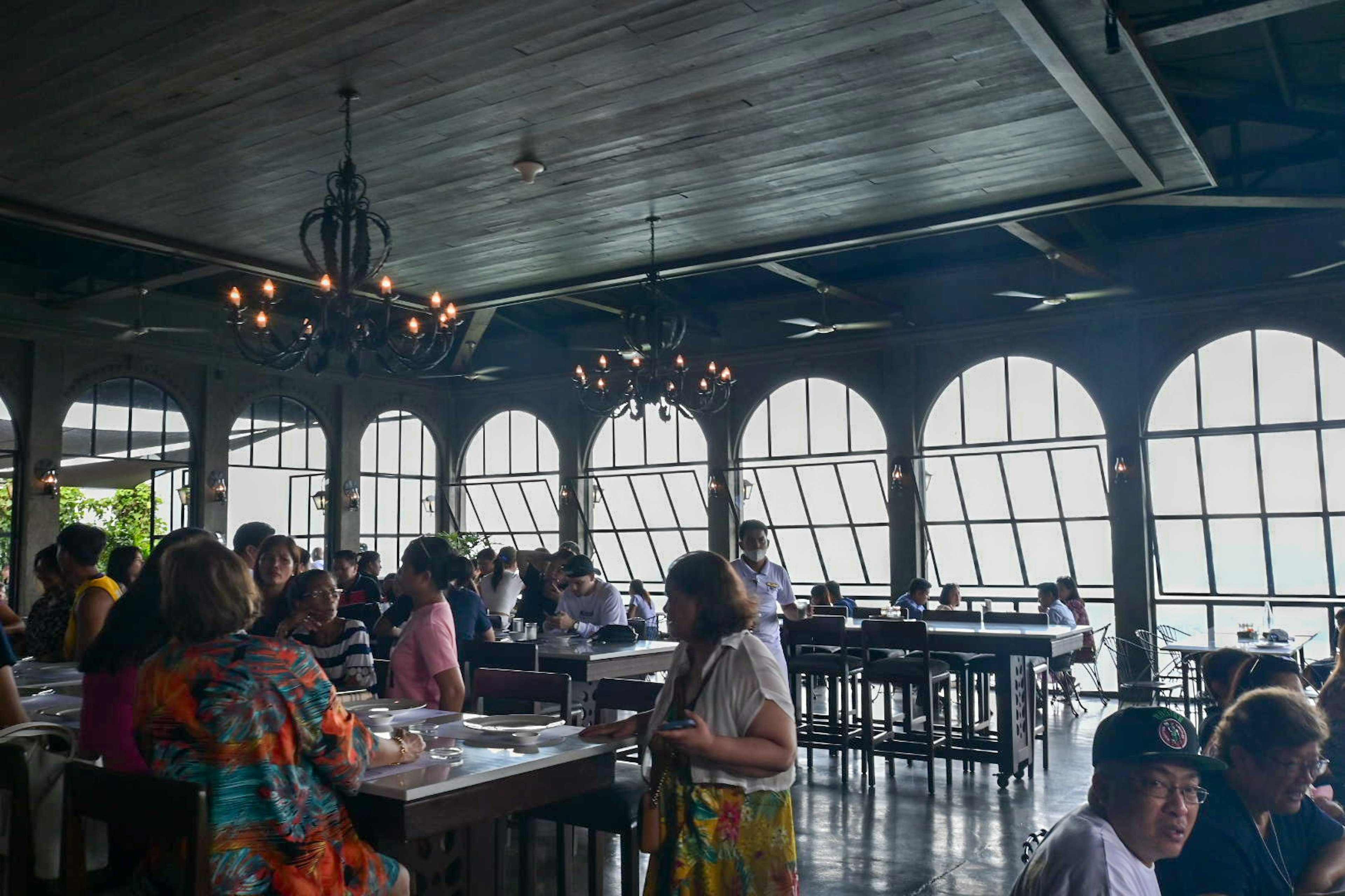 Bagian dalam restoran dengan jendela besar dan banyak orang yang makan