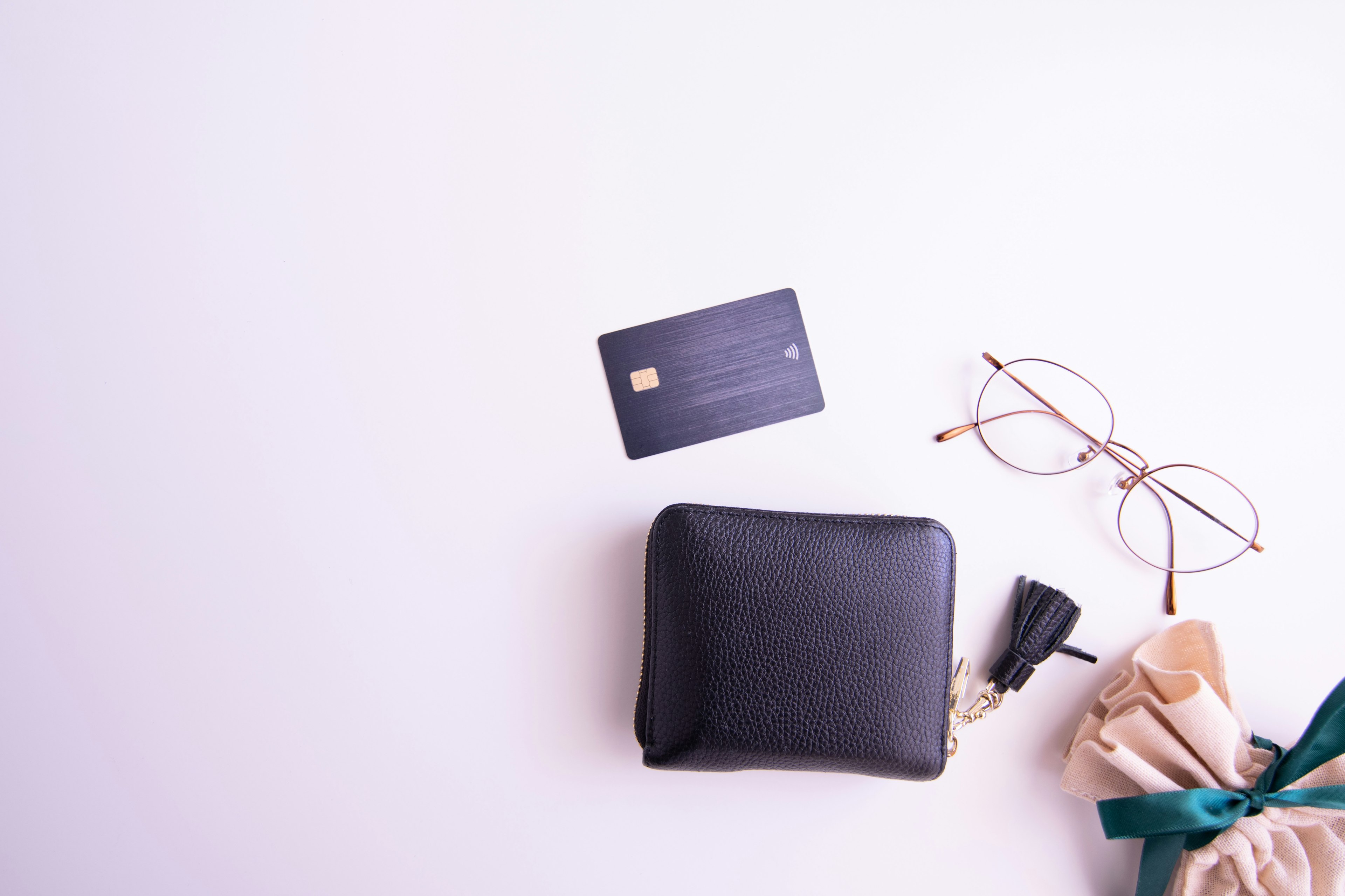 A black wallet with a credit card glasses and wrapped gift with a ribbon on a simple desk