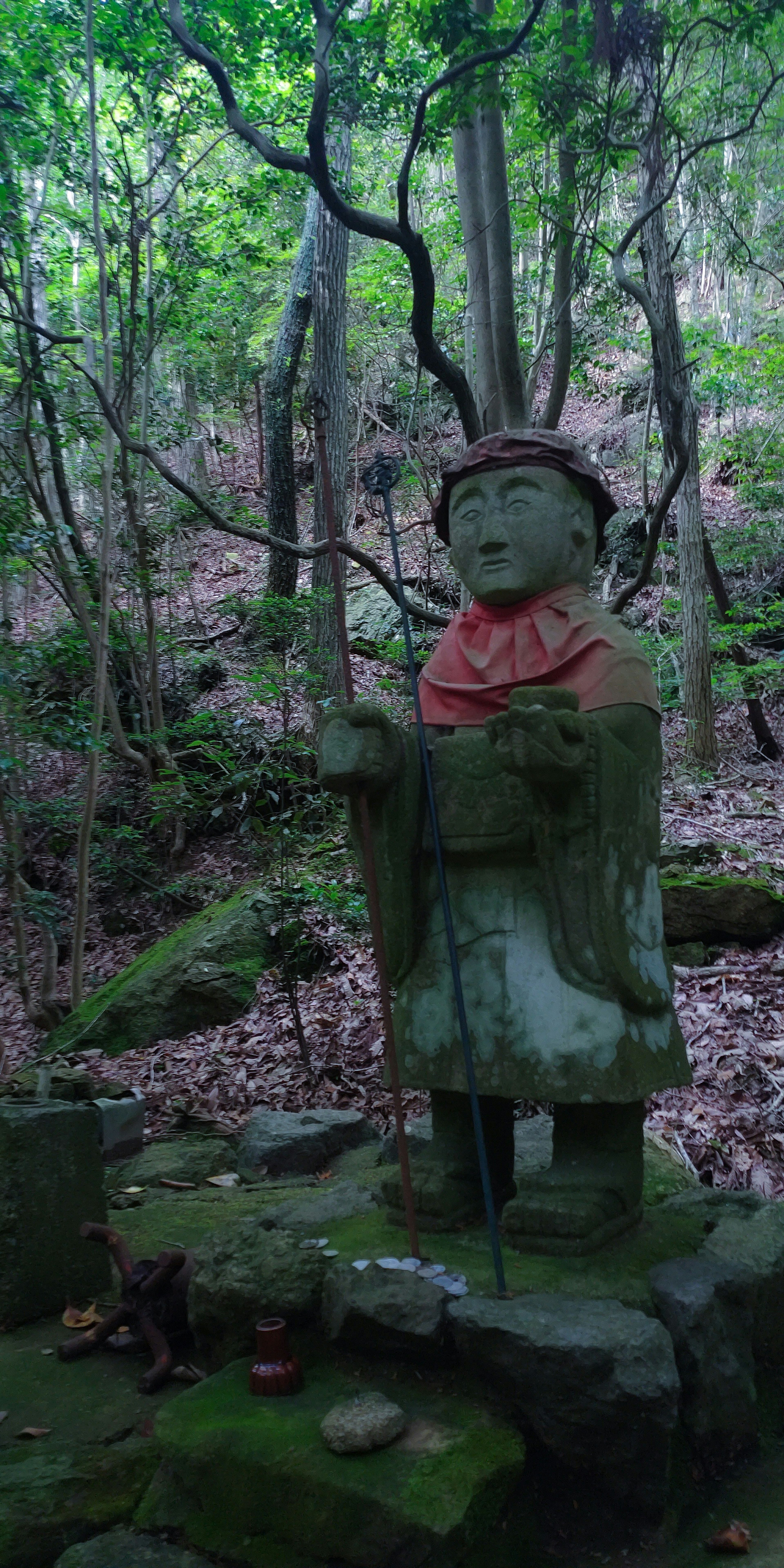 Steinstatue steht in einem grünen Wald mit einem roten Schal