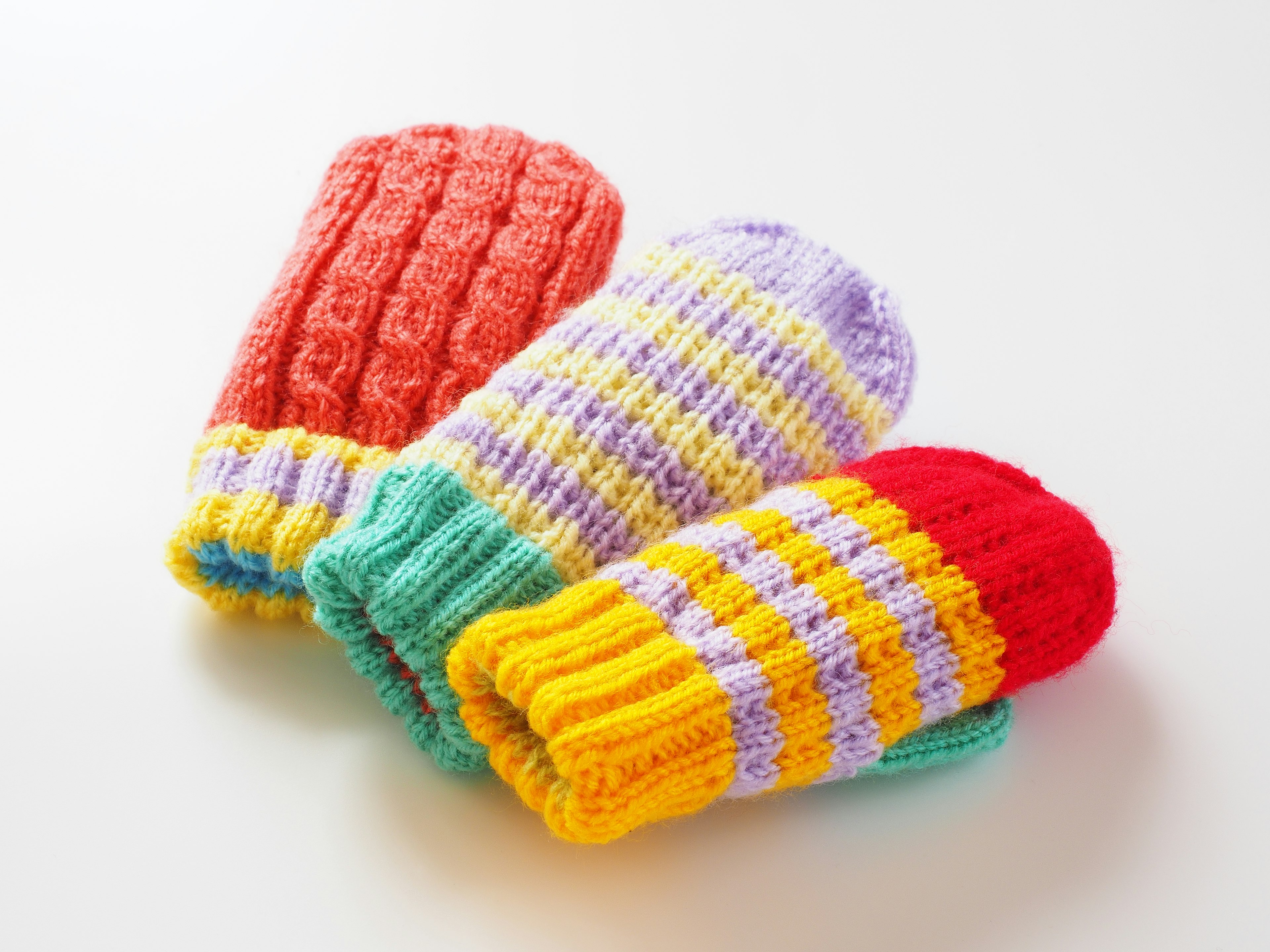 Three colorful mittens arranged together featuring red, purple, and yellow striped designs