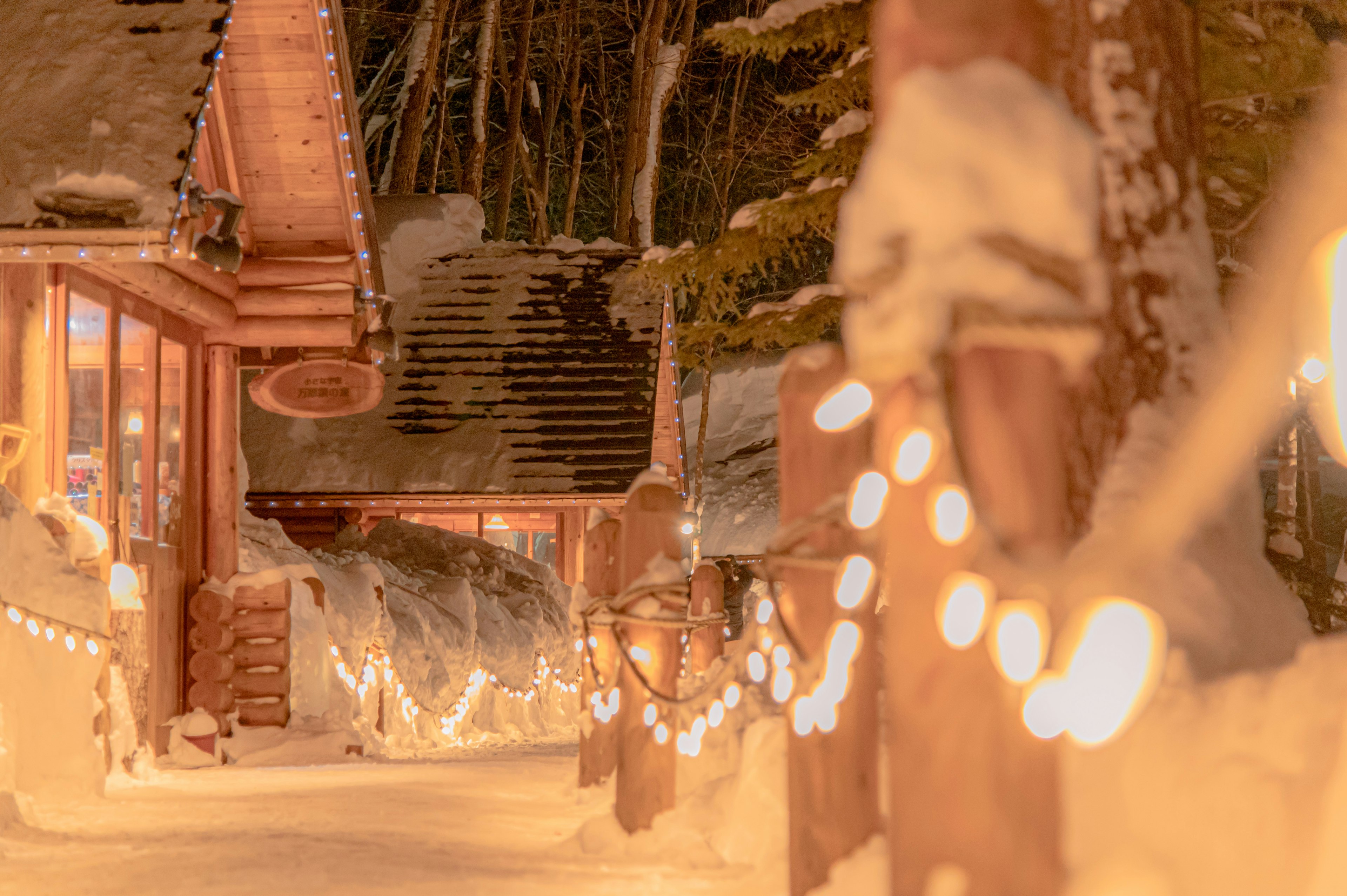 Escena invernal con luces brillantes a lo largo de un camino cubierto de nieve y cabañas de troncos