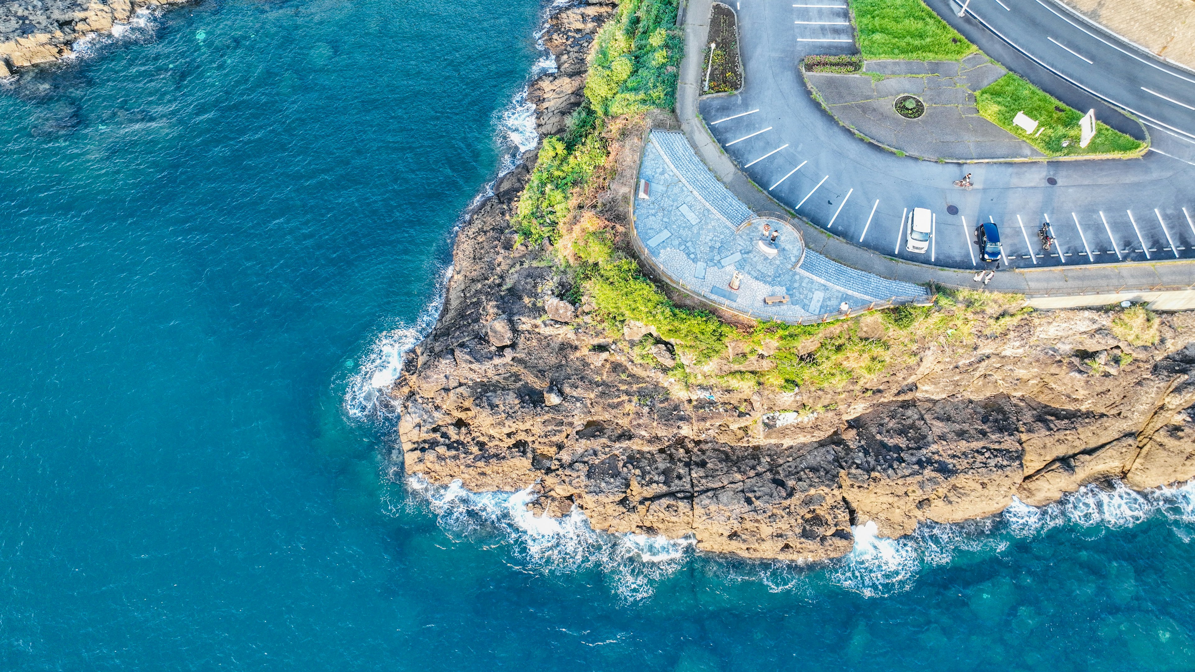 青い海と岩の岬が見える空撮画像 駐車場と緑のスペースがある