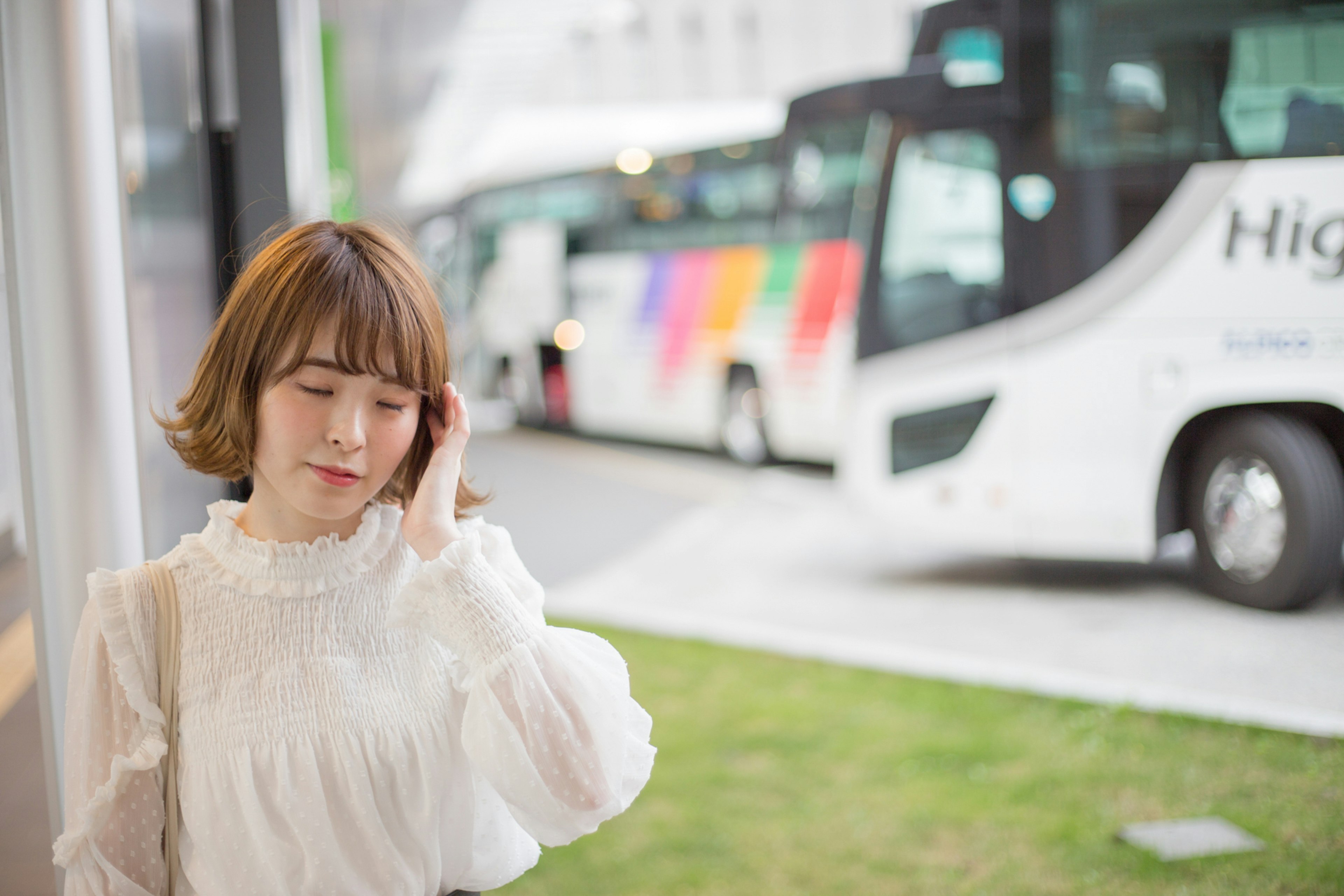 Portrait d'une femme se tenant avec des bus en arrière-plan portant un chemisier blanc et ayant une expression légèrement troublée