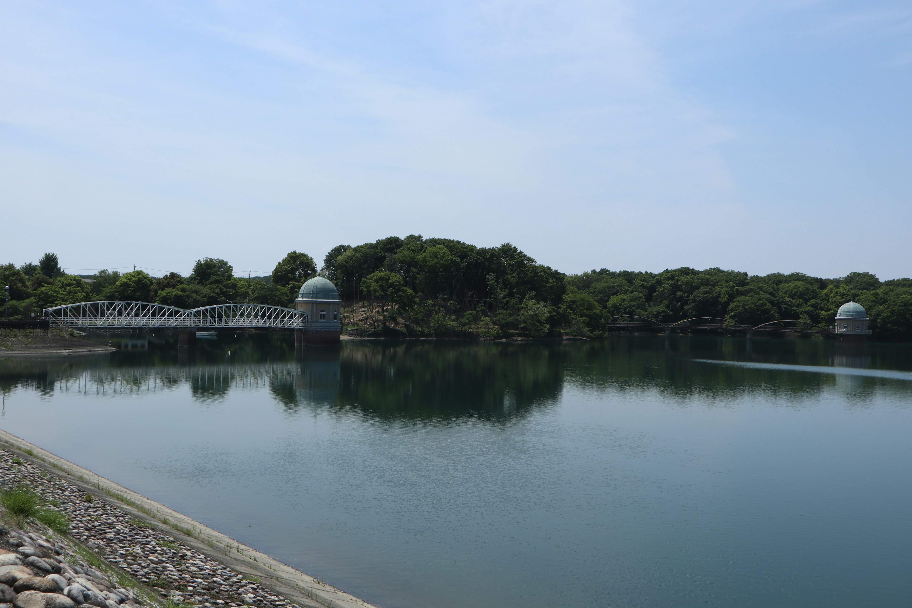 Danau tenang dengan tepi hijau yang rimbun dan dua struktur berbentuk kubah