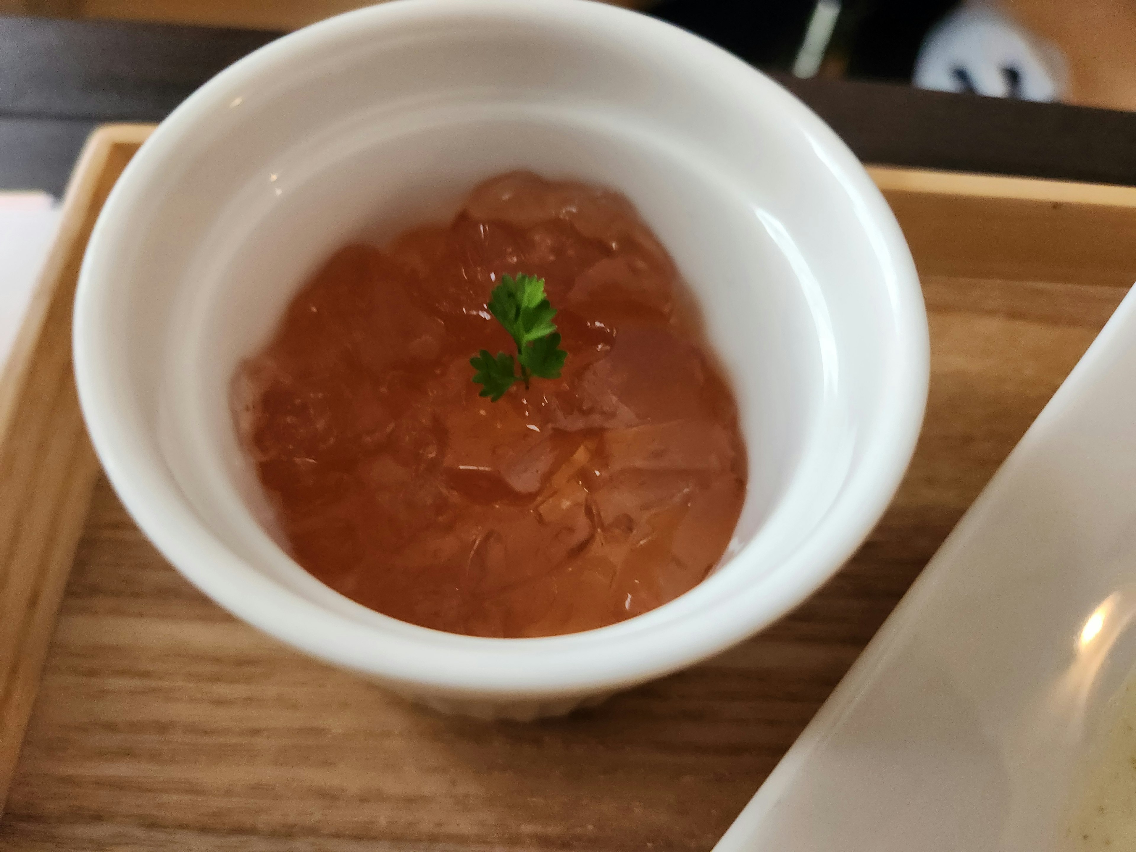 Dish in a white cup containing reddish food garnished with parsley