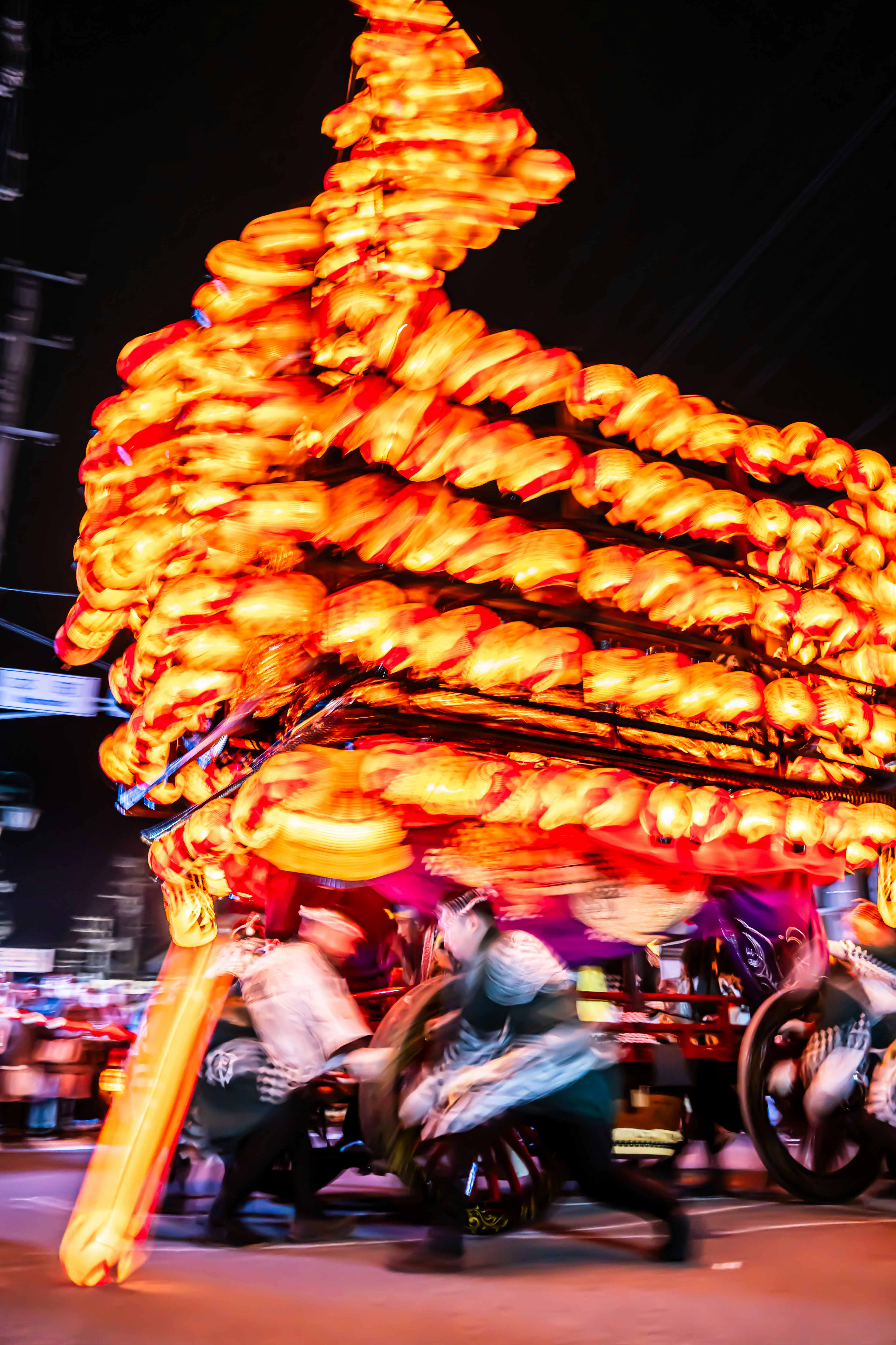 Menschen ziehen einen hell erleuchteten orangefarbenen Wagen während eines Nachtfestes