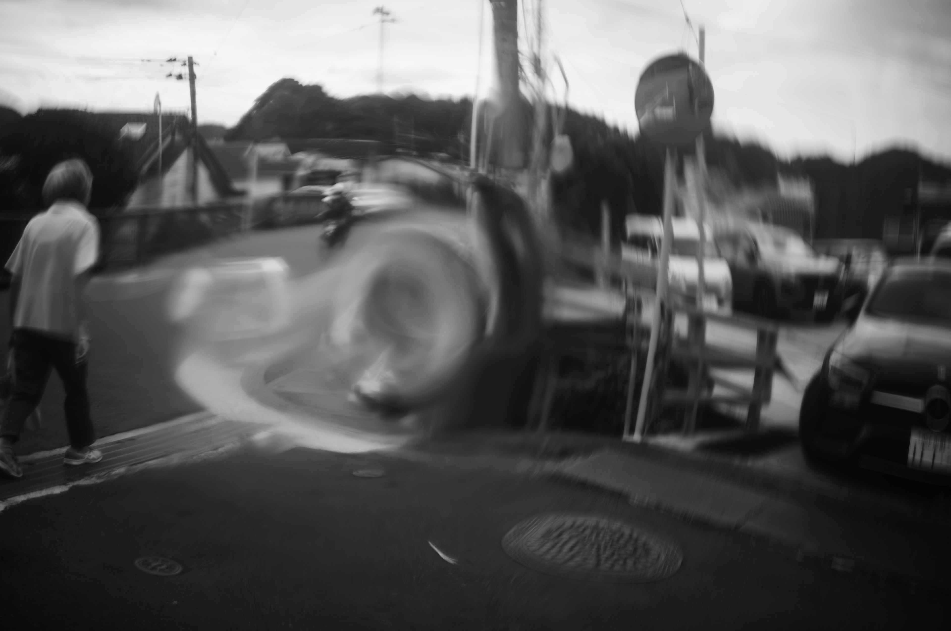 Escena de calle borrosa con una persona de pie y un coche que pasa en blanco y negro