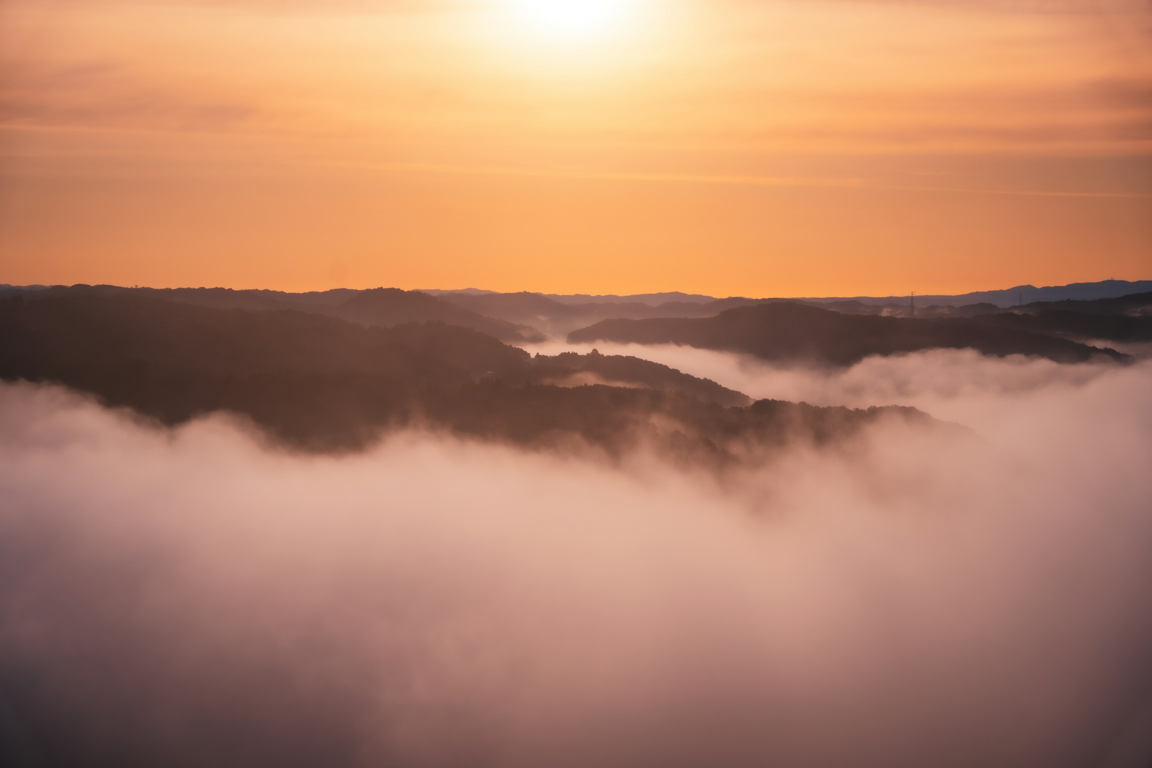 Montañas en silueta envueltas en niebla con un cálido resplandor del atardecer