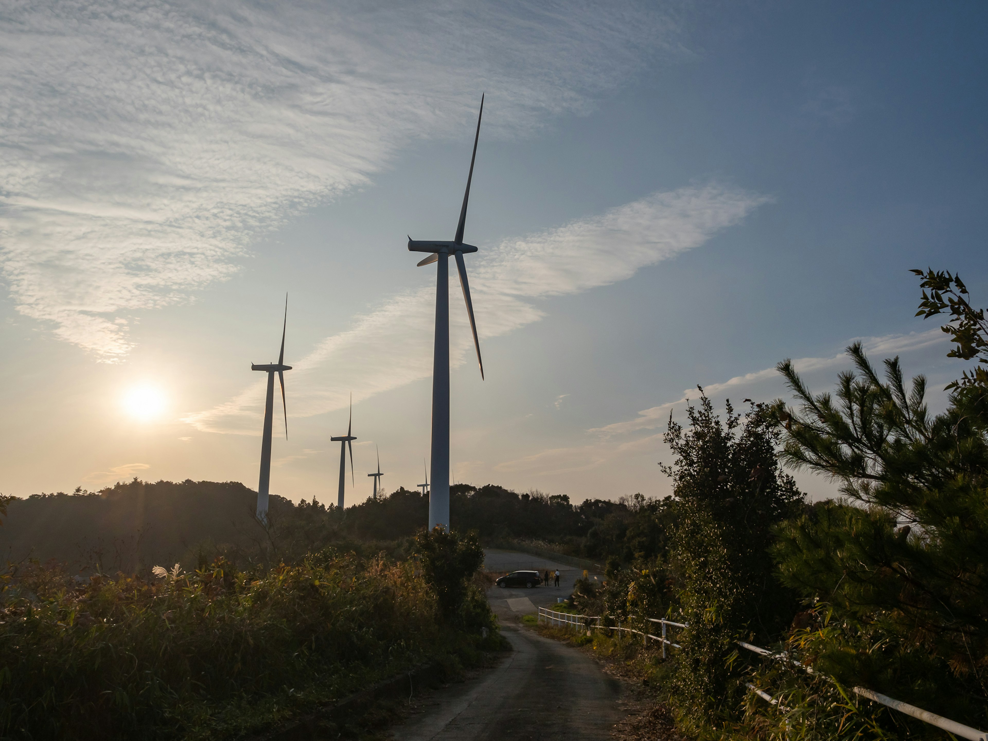 Landschaft mit Windkraftanlagen entlang eines Weges mit Sonnenuntergang im Hintergrund