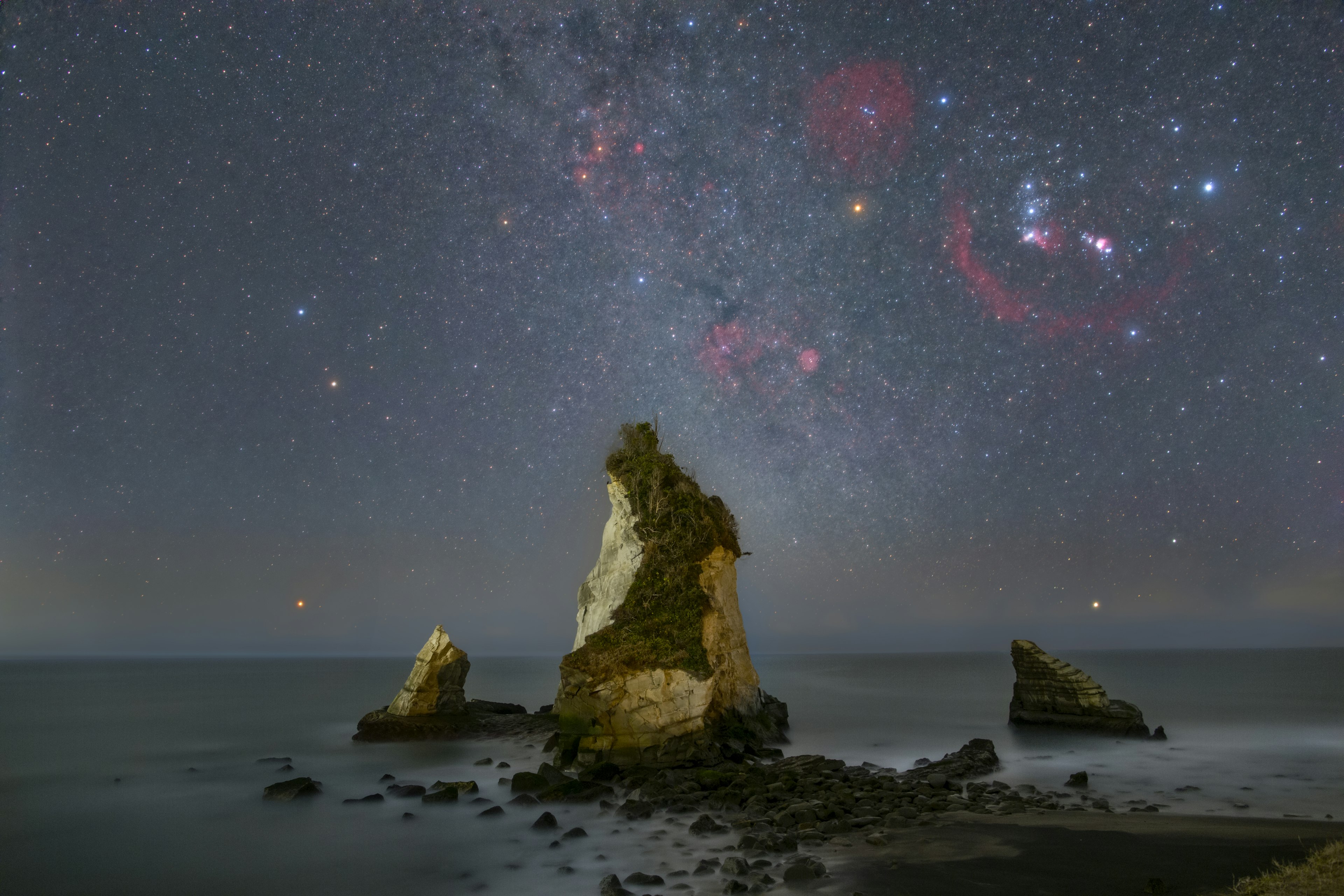 夜空に広がる星々と海に浮かぶ岩の風景