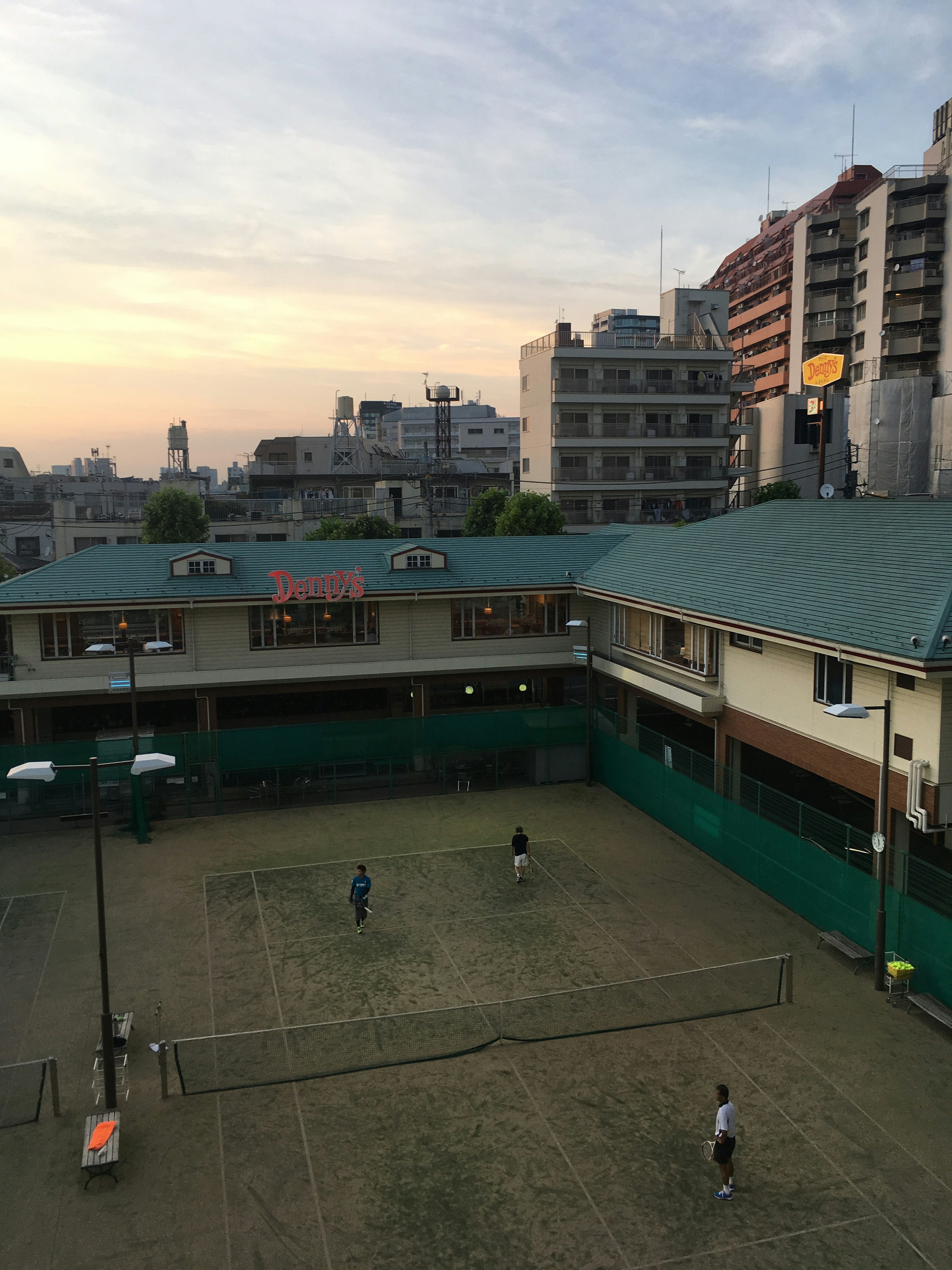 Players playing on a tennis court during sunset