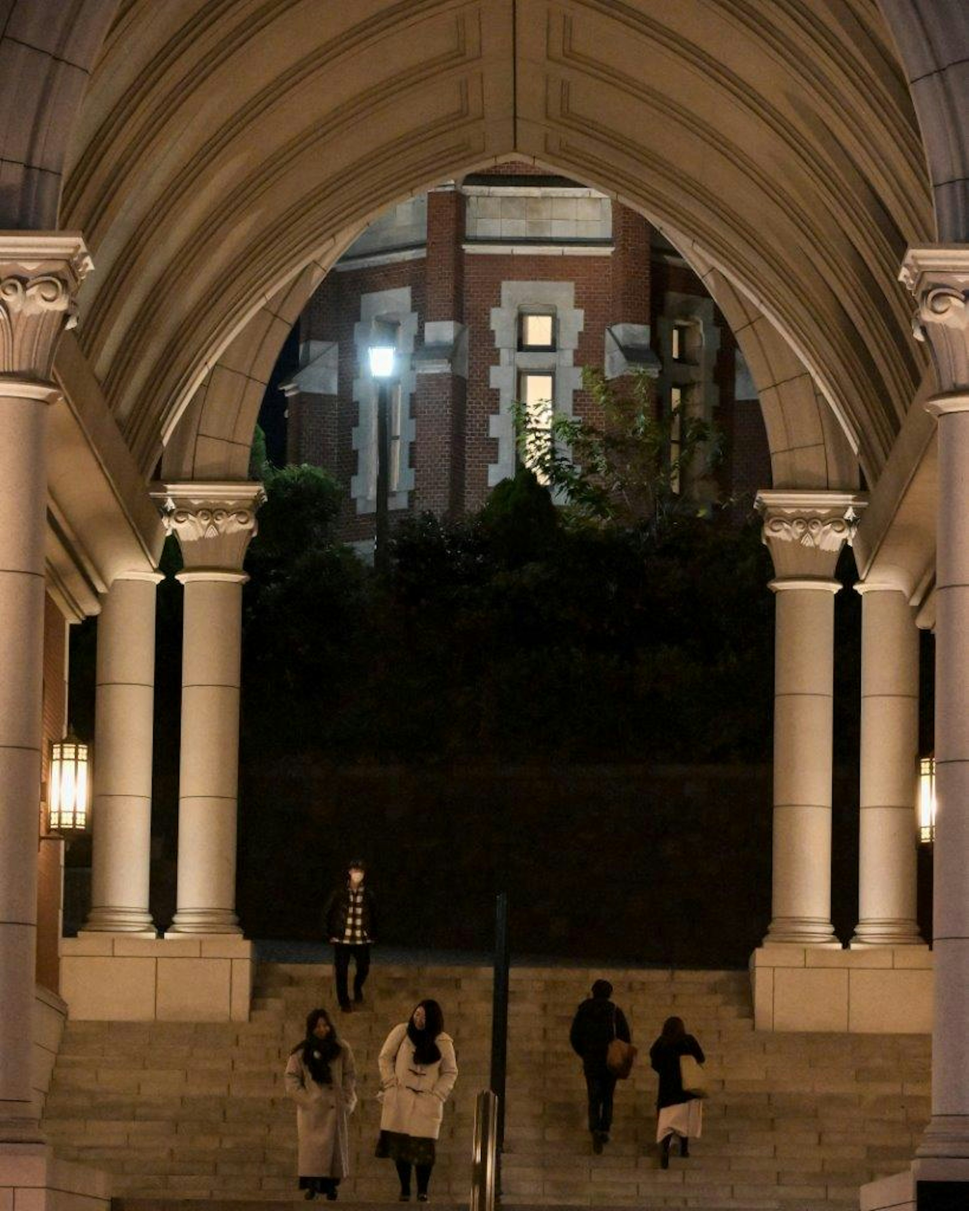 People walking through an archway at night with a building in the background