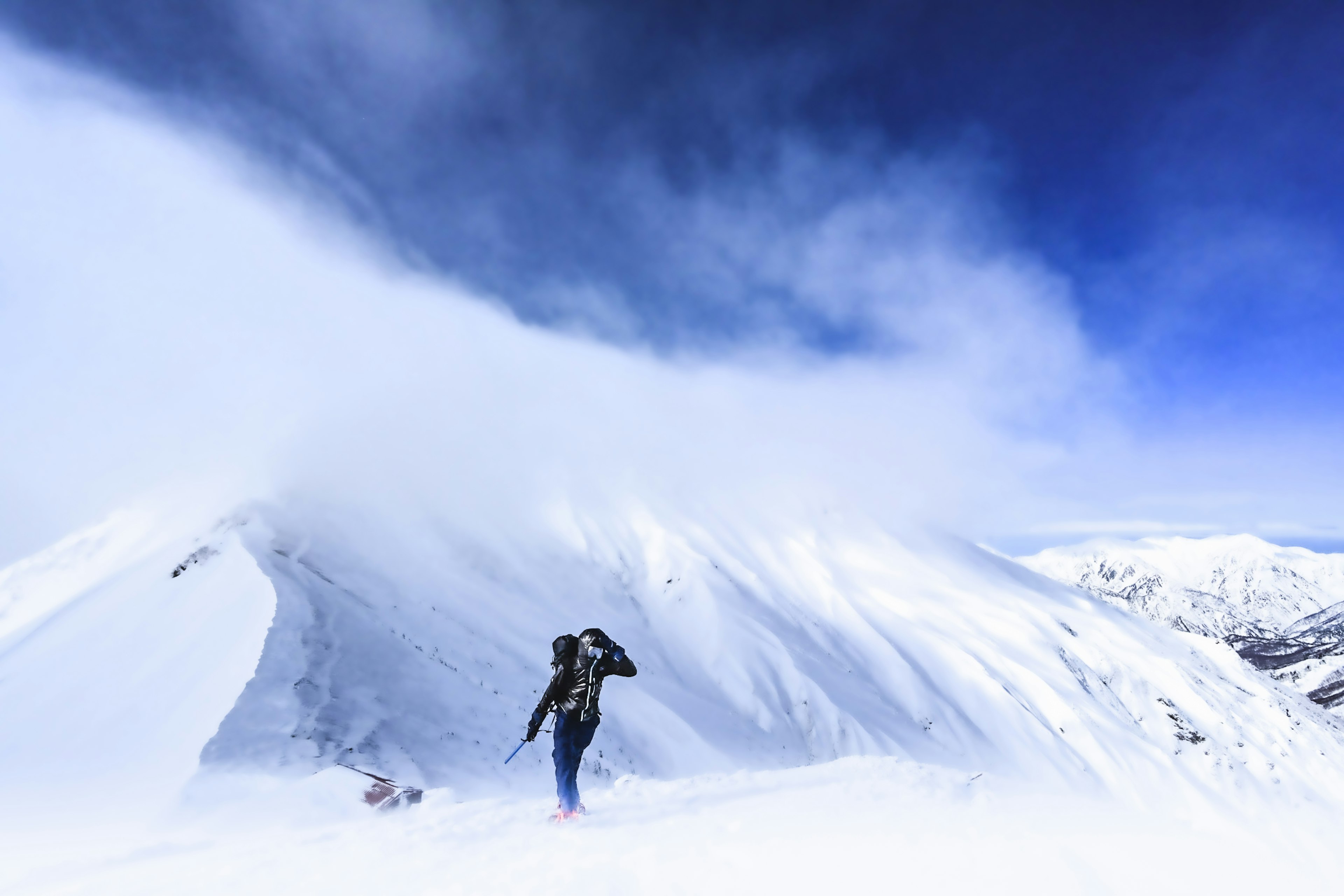 Senderista escalando una montaña nevada bajo un cielo azul nublado cubierto de nieve blanca