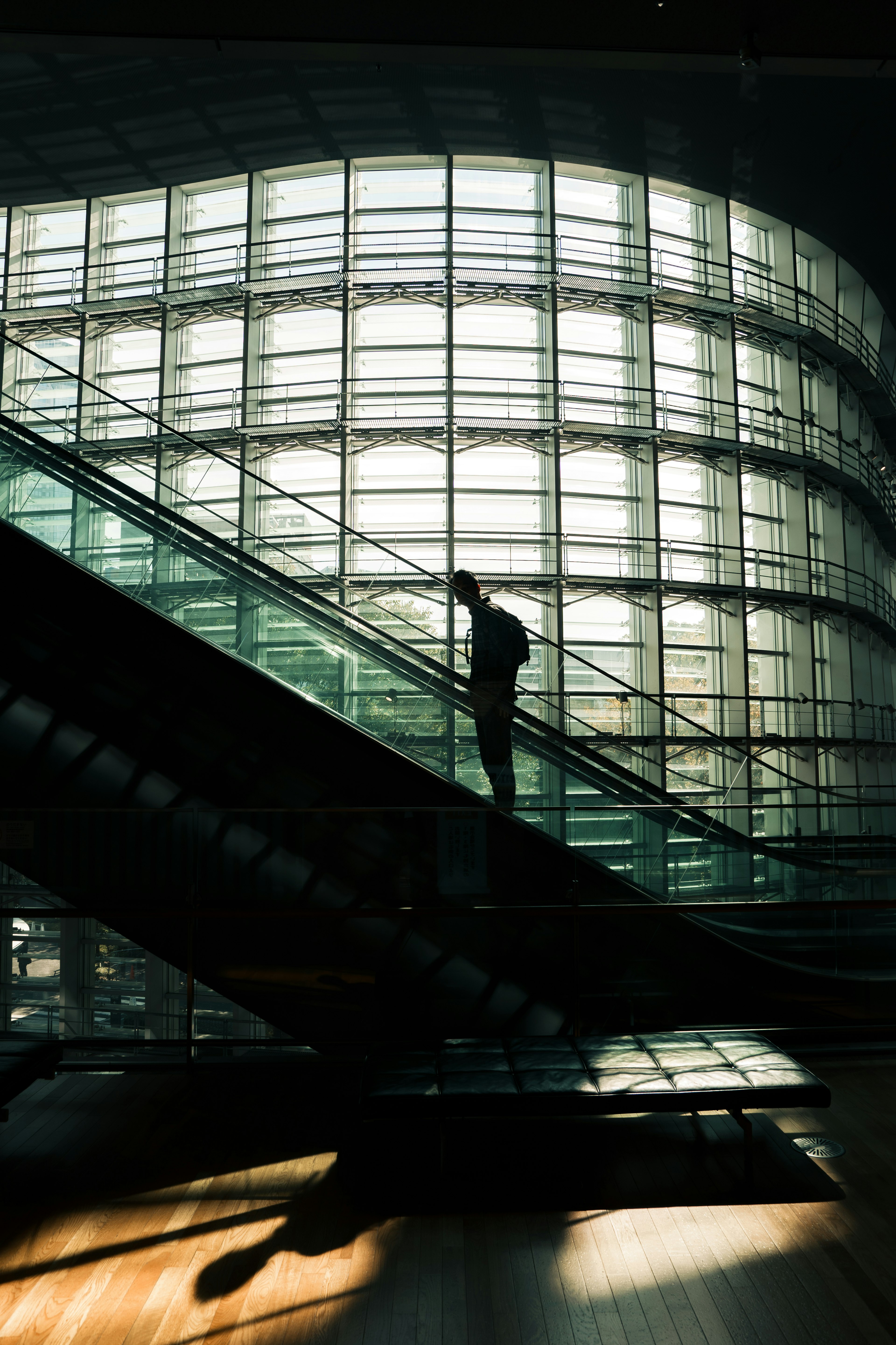 Silhouette of a person ascending an escalator with a modern glass building