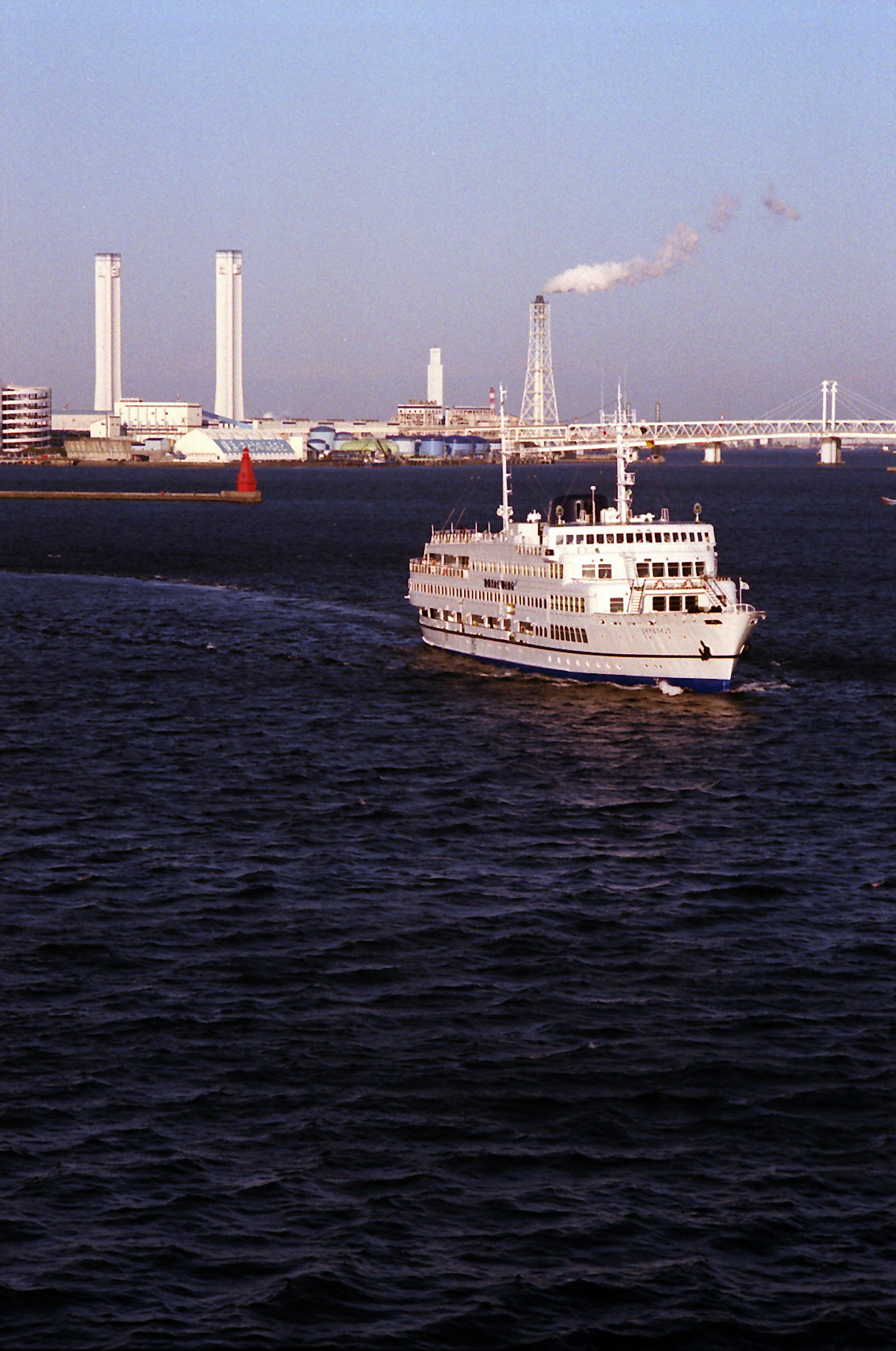 Ein weißes Schiff fährt auf dem Meer mit Fabriken, die Rauch im Hintergrund ausstoßen