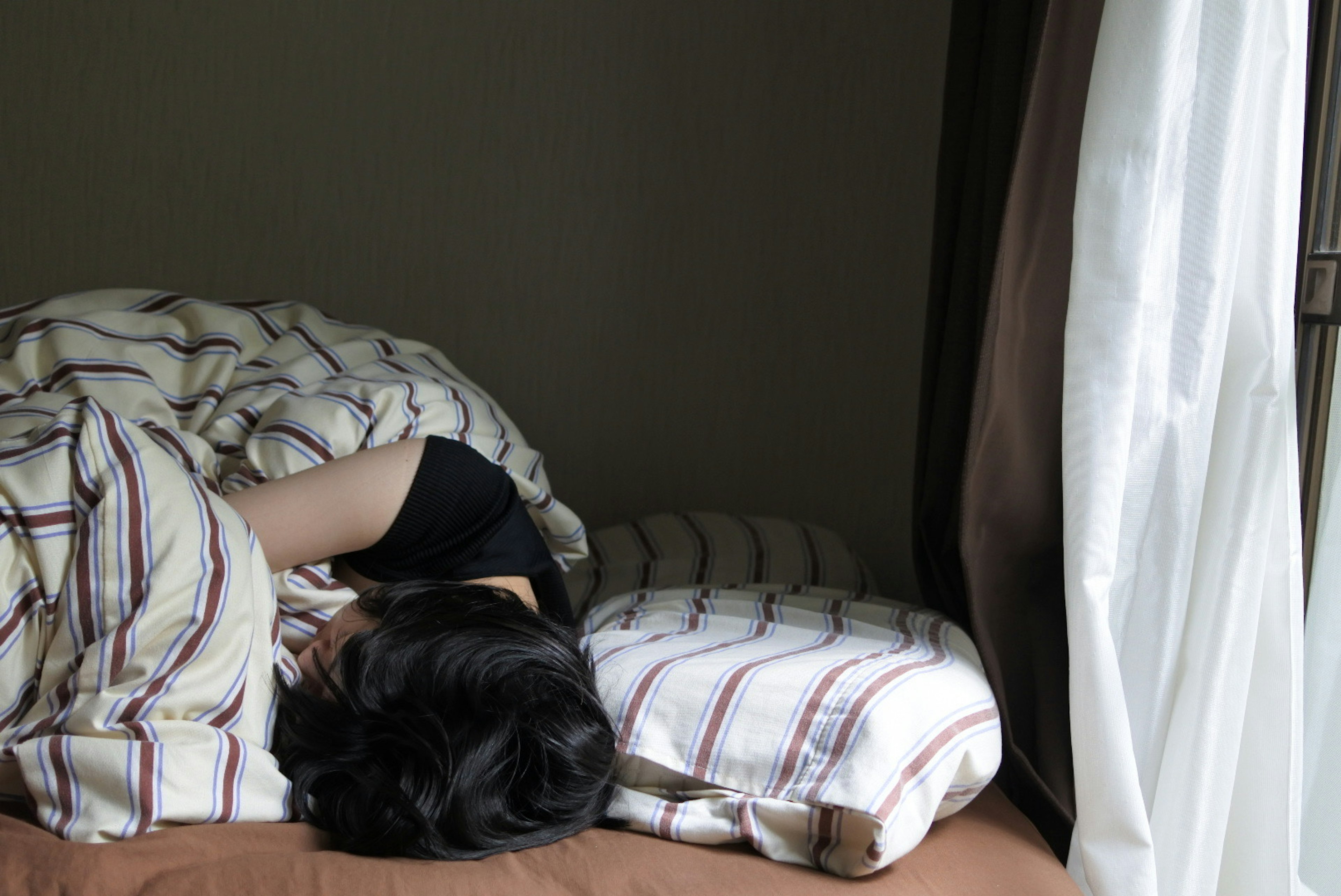 Woman lying on bed covered with a striped blanket