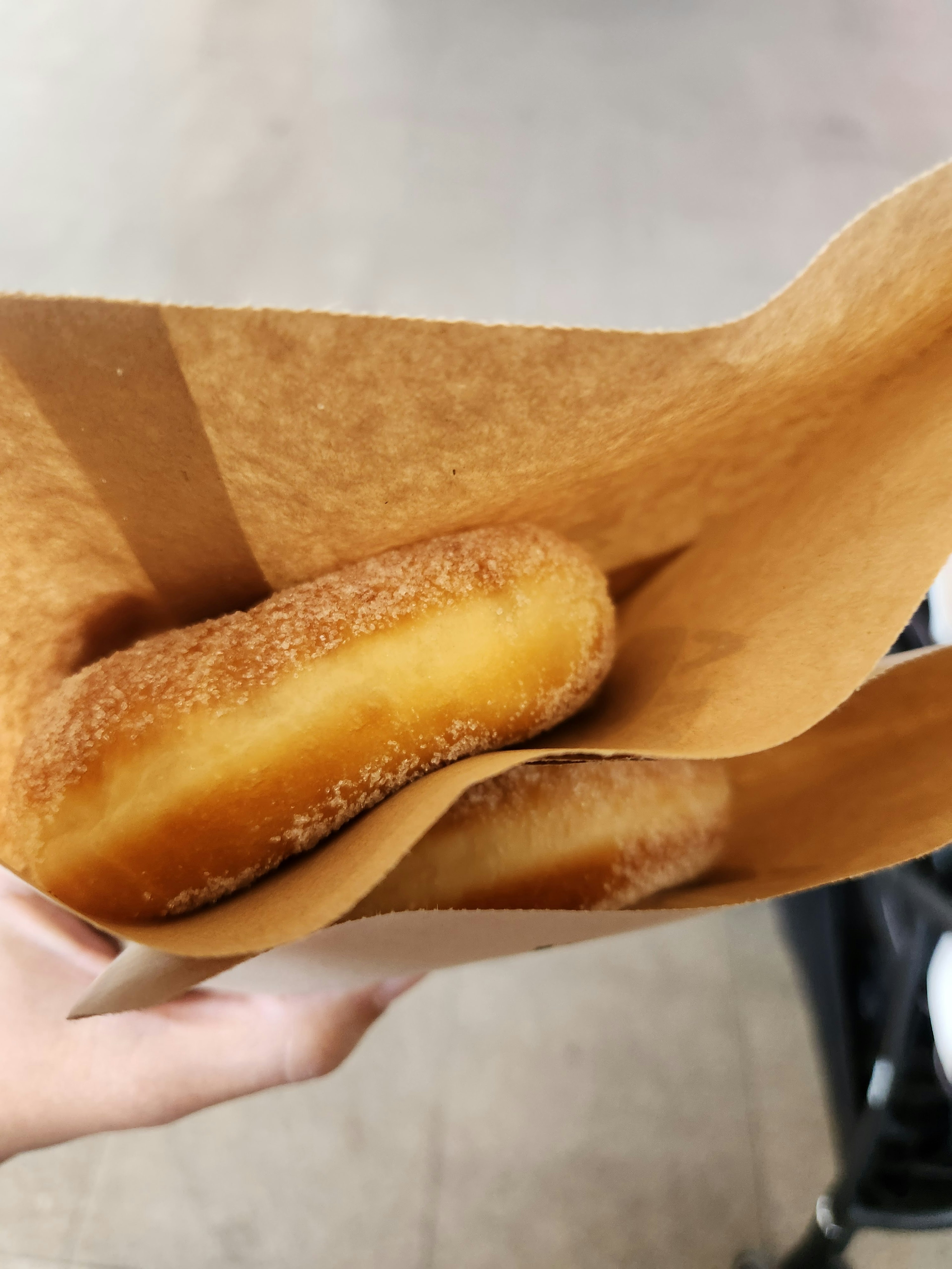 Two donuts held in hand with brown paper wrapping