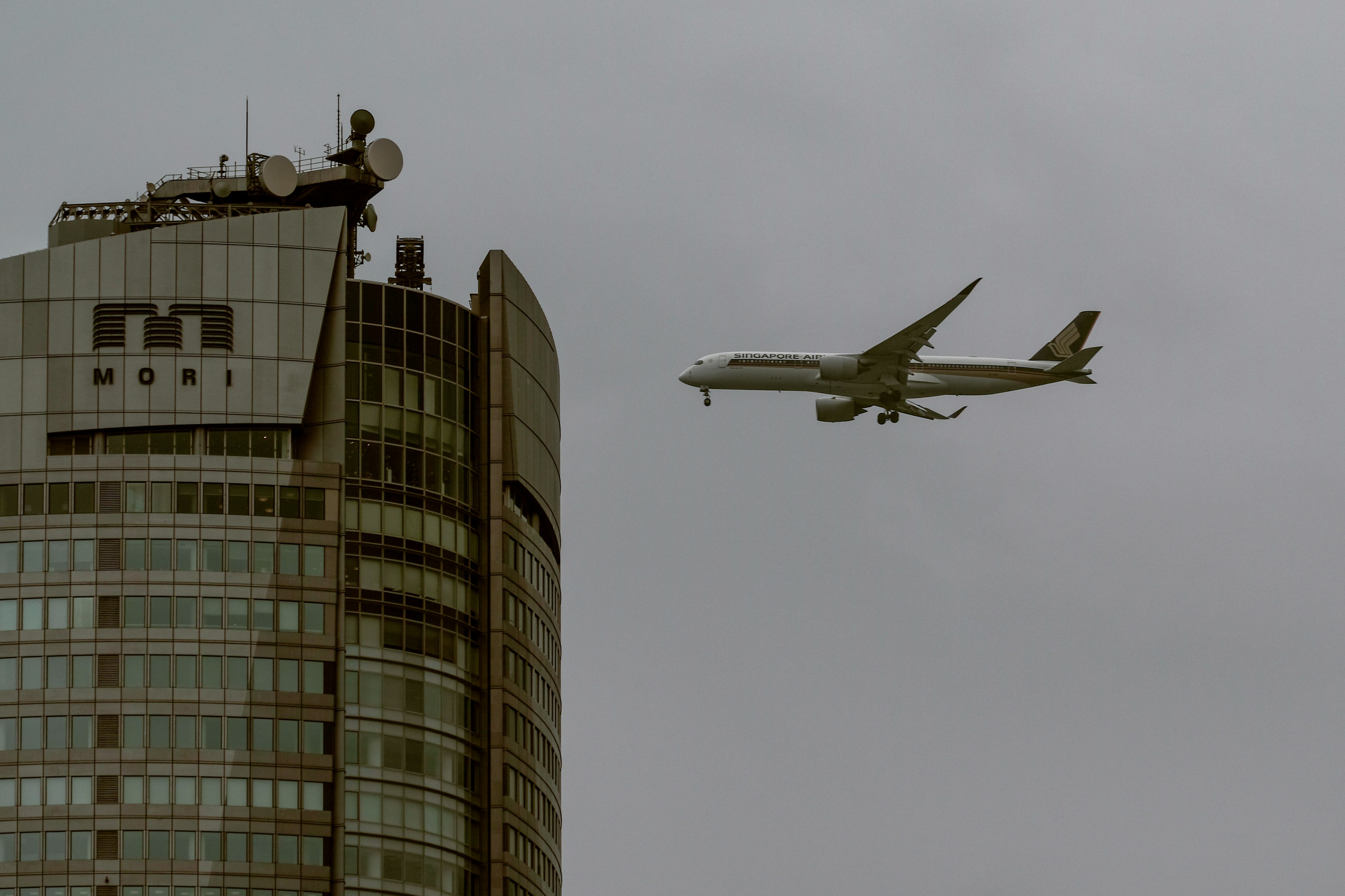 Airplane flying near a skyscraper under a cloudy sky