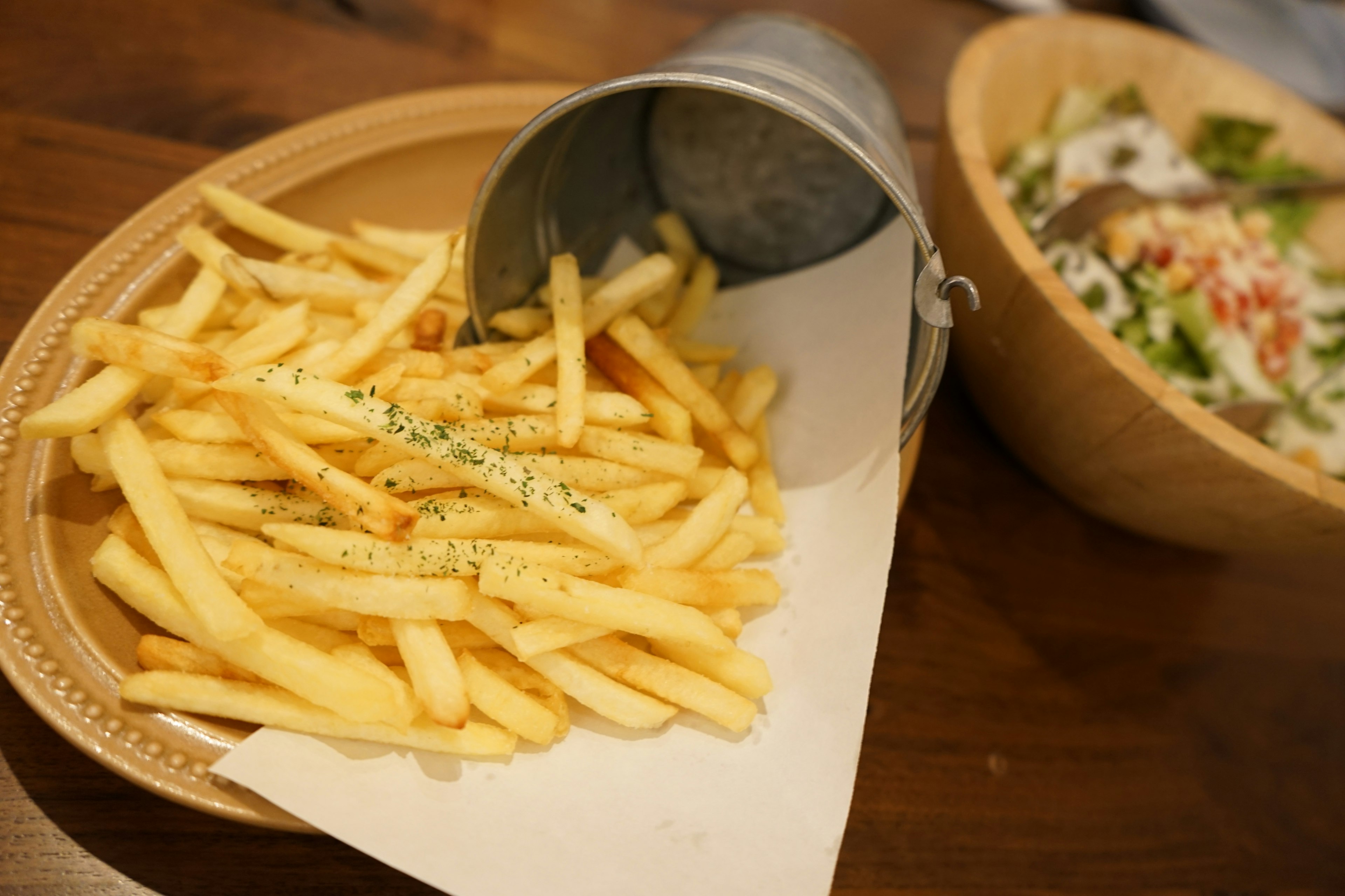 Piatto di patatine fritte servito con una ciotola di insalata sullo sfondo