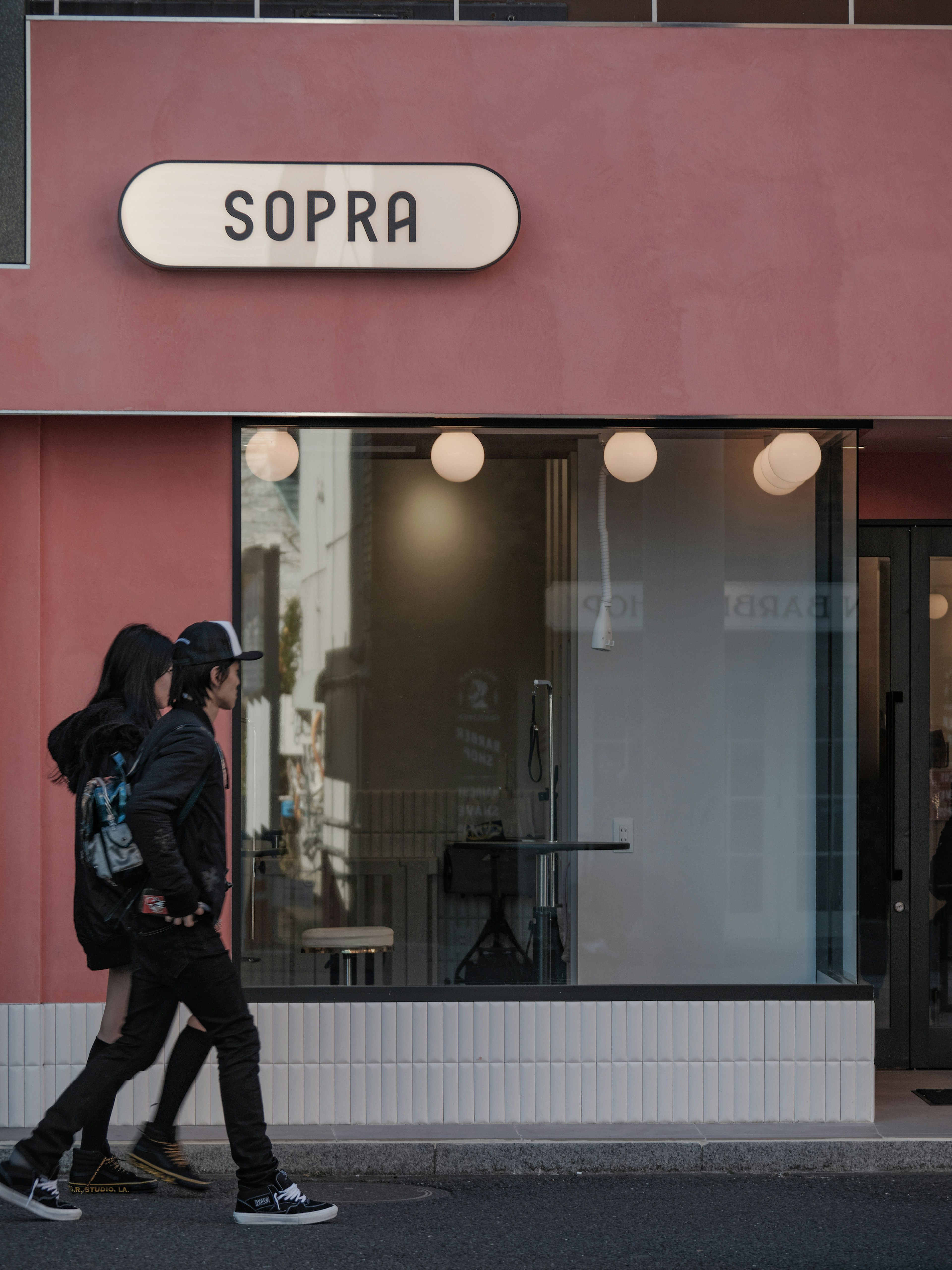 Two people walking in front of the pink exterior cafe SOPRA