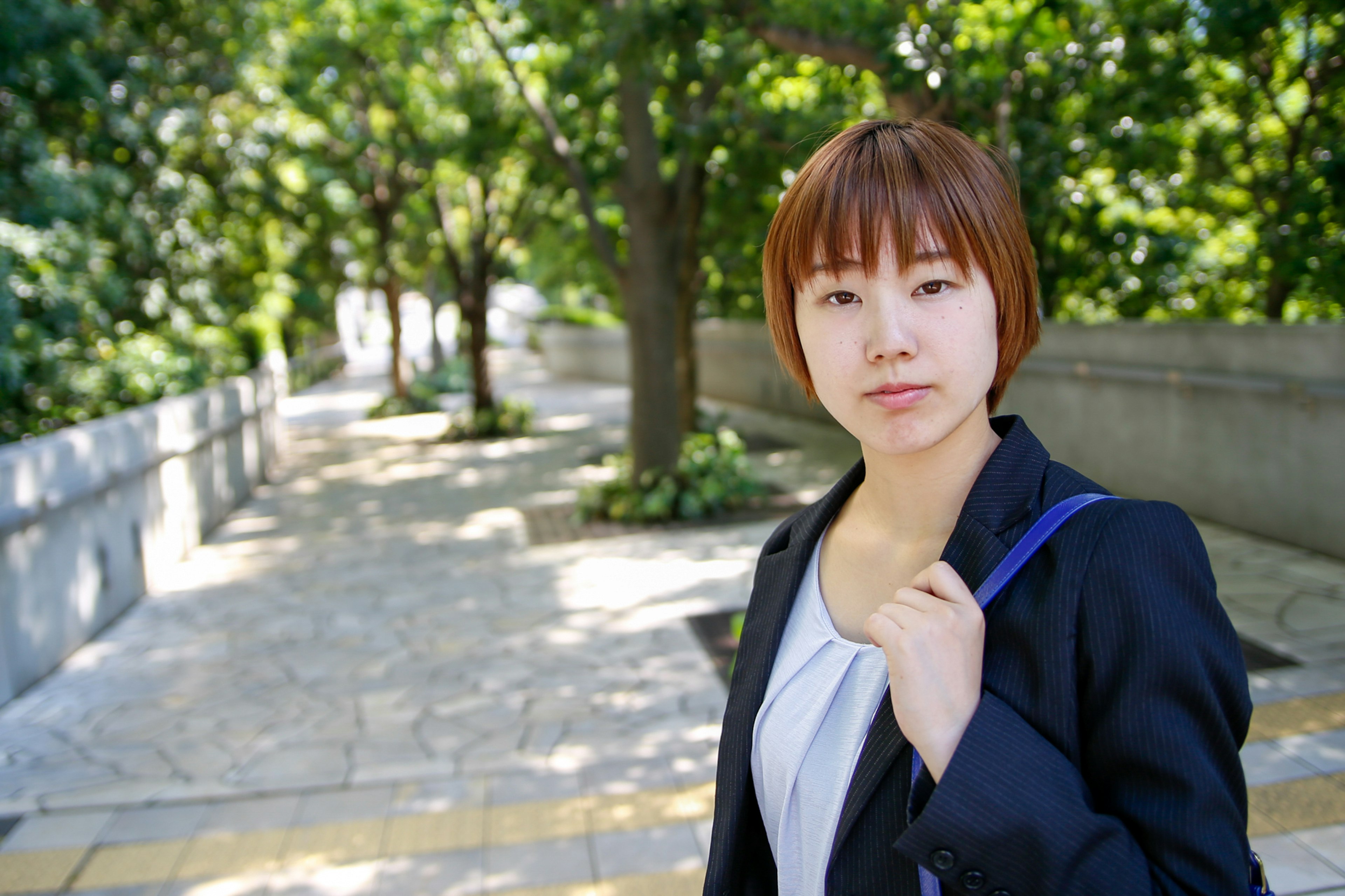 Portrait of a woman standing on a park path surrounded by green trees