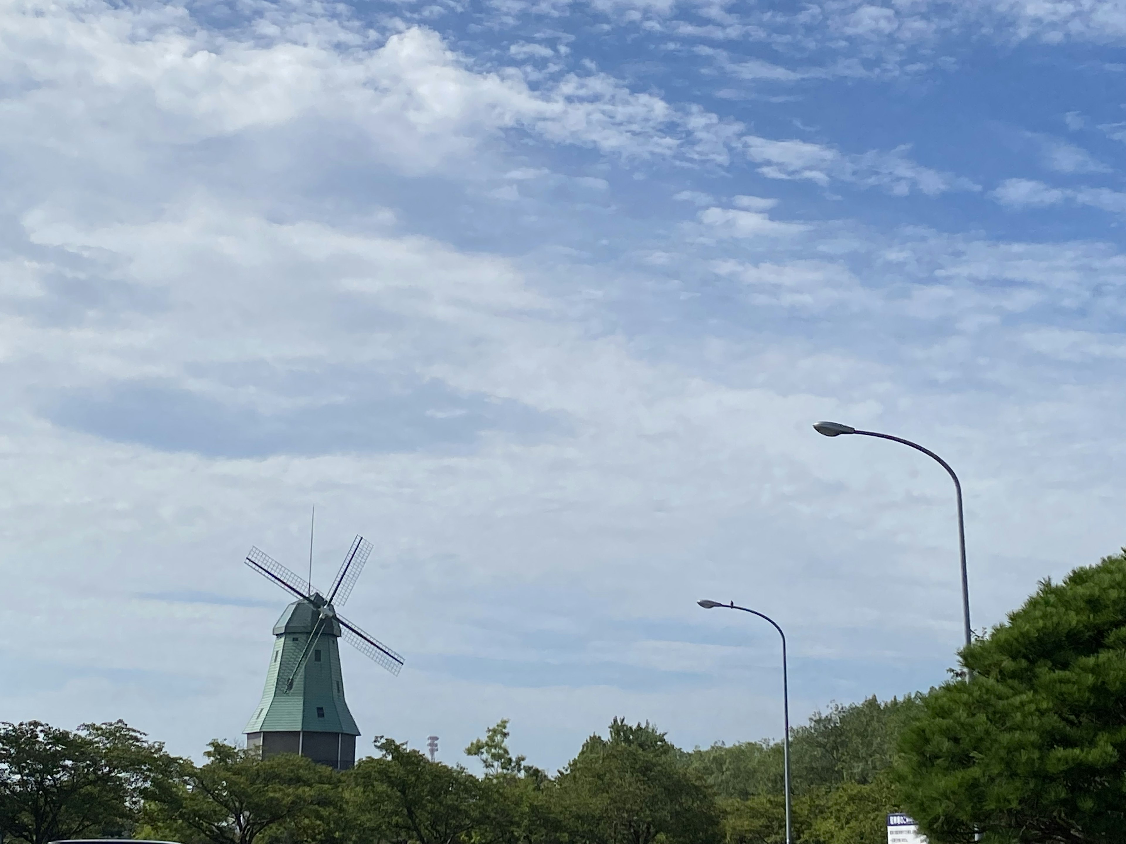 Windmill under a blue sky with surrounding green trees