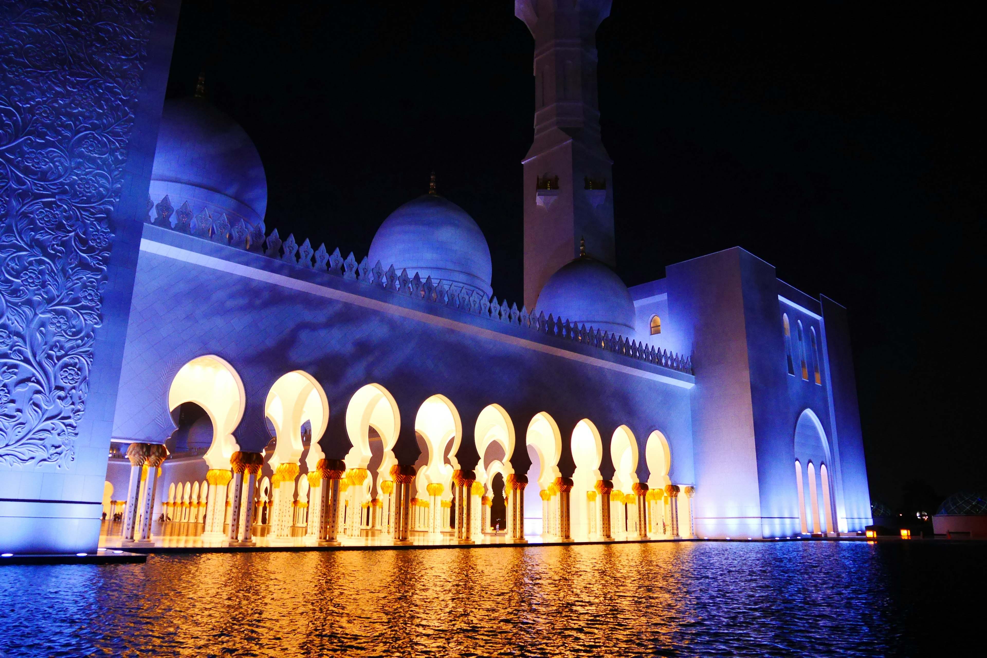 Mezquita Sheikh Zayed iluminada por la noche con arcos y reflejos