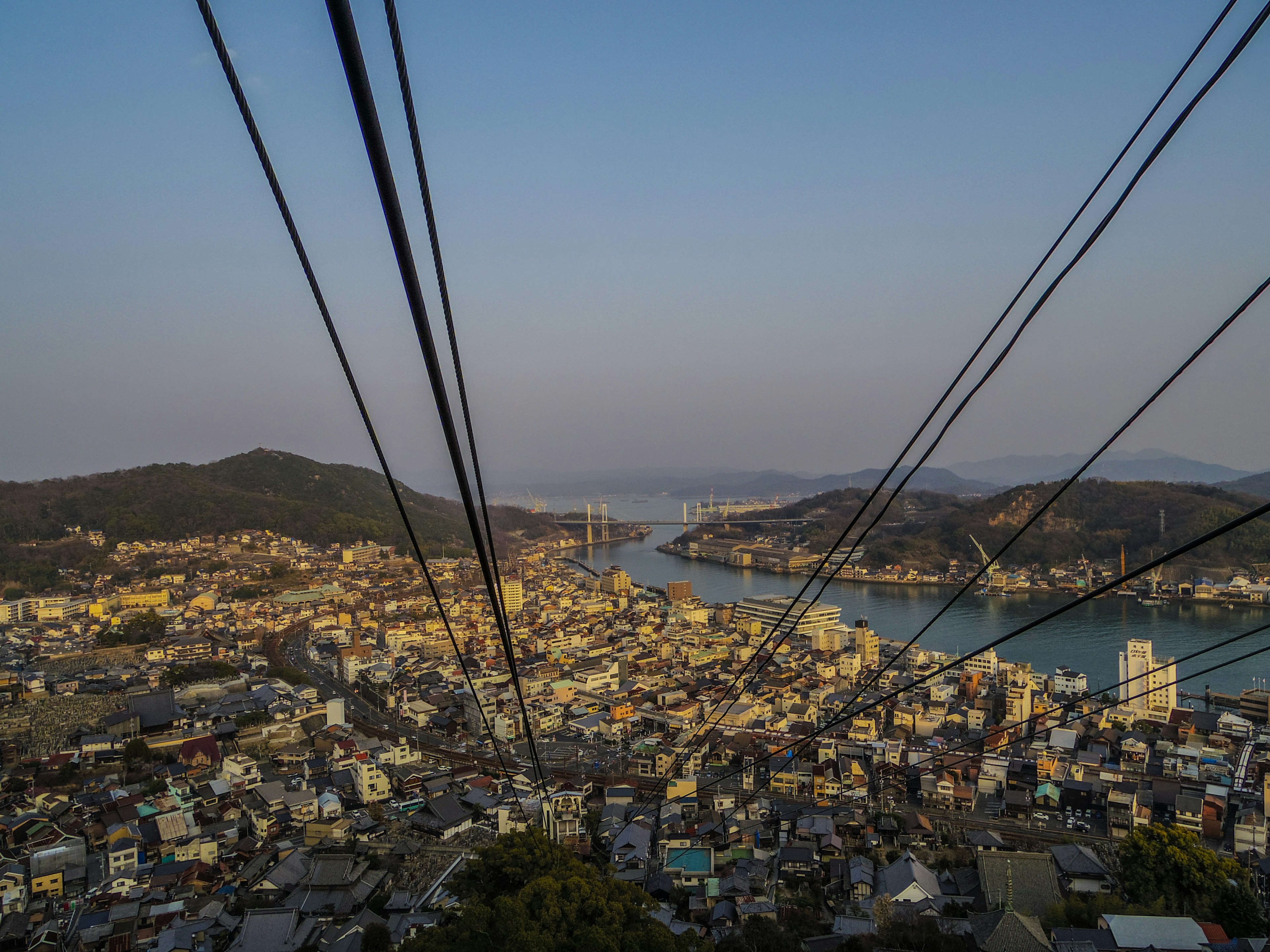 Vue panoramique d'une ville et de la mer depuis un sommet de montagne avec des câbles de téléphérique au premier plan